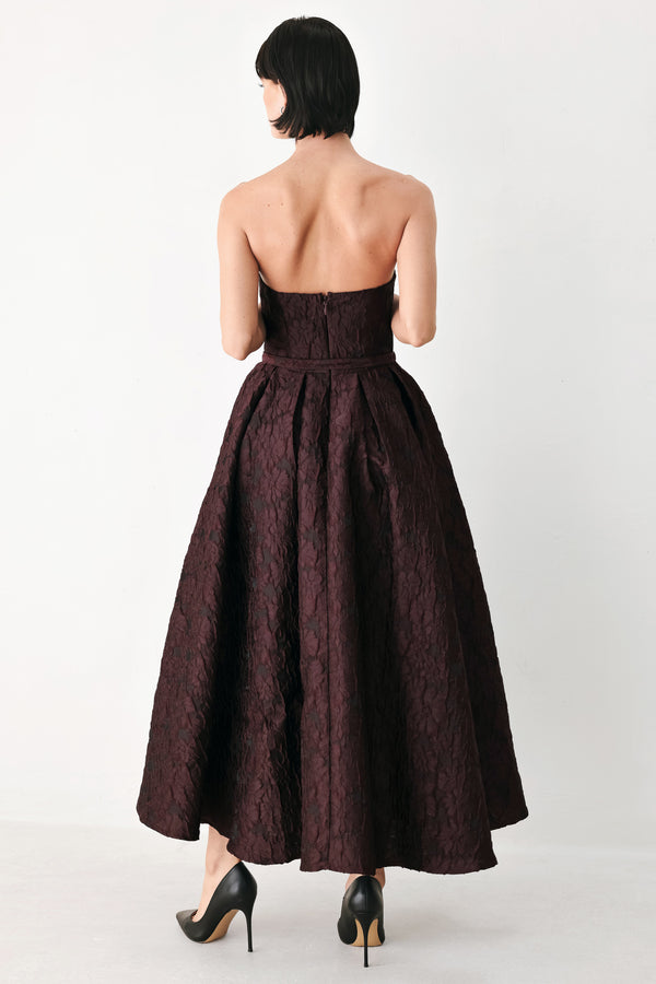 A woman models a strapless burgundy A-line gown with a textured jacquard bodice and a matching beaded waistband | FREEMARKET