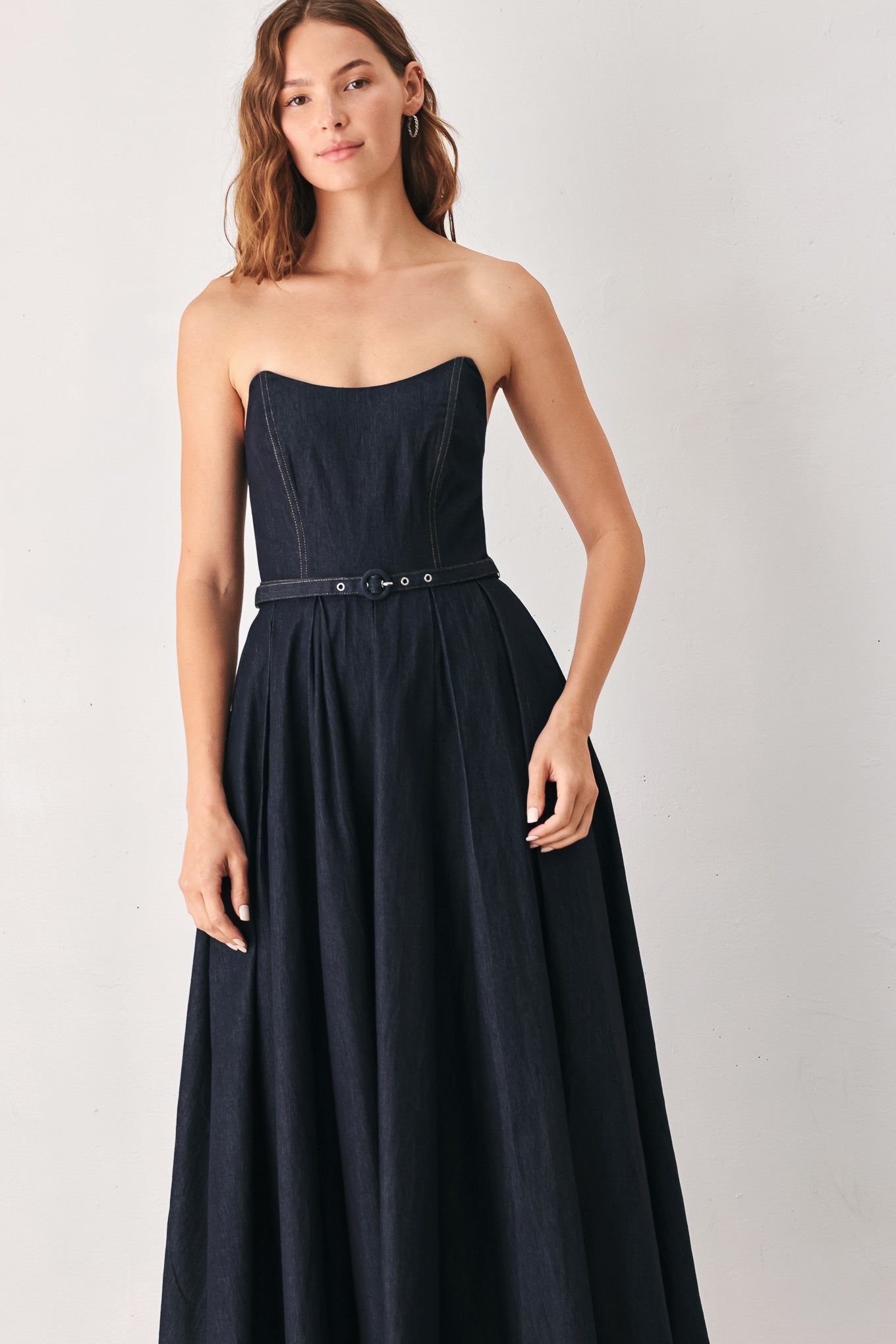 A woman wearing a strapless midi dress in dark navy blue with a matching belt | FREEMARKET