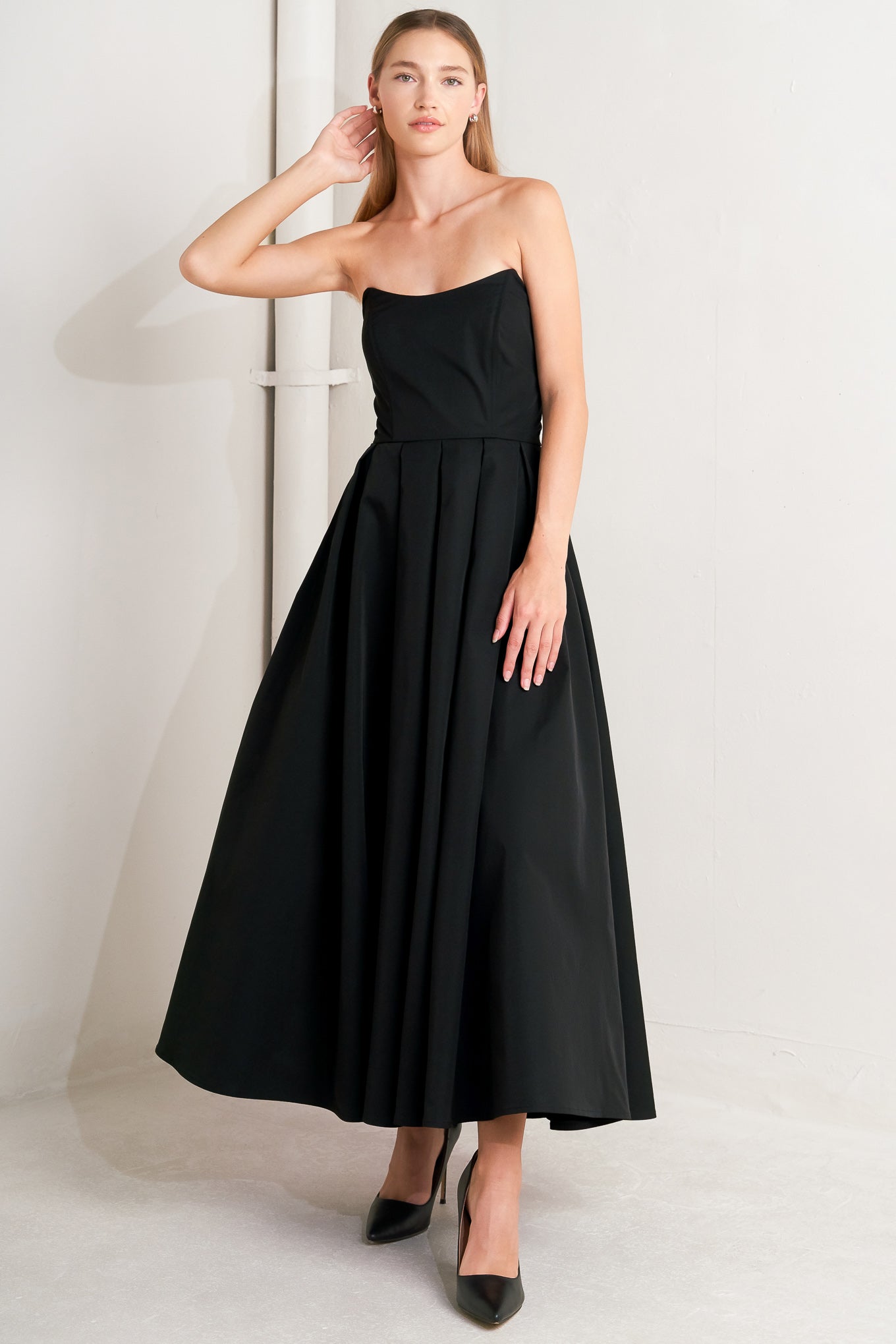 A solid woven midi dress featuring strapless with pointed side neckline, full skirt and back zipper closure