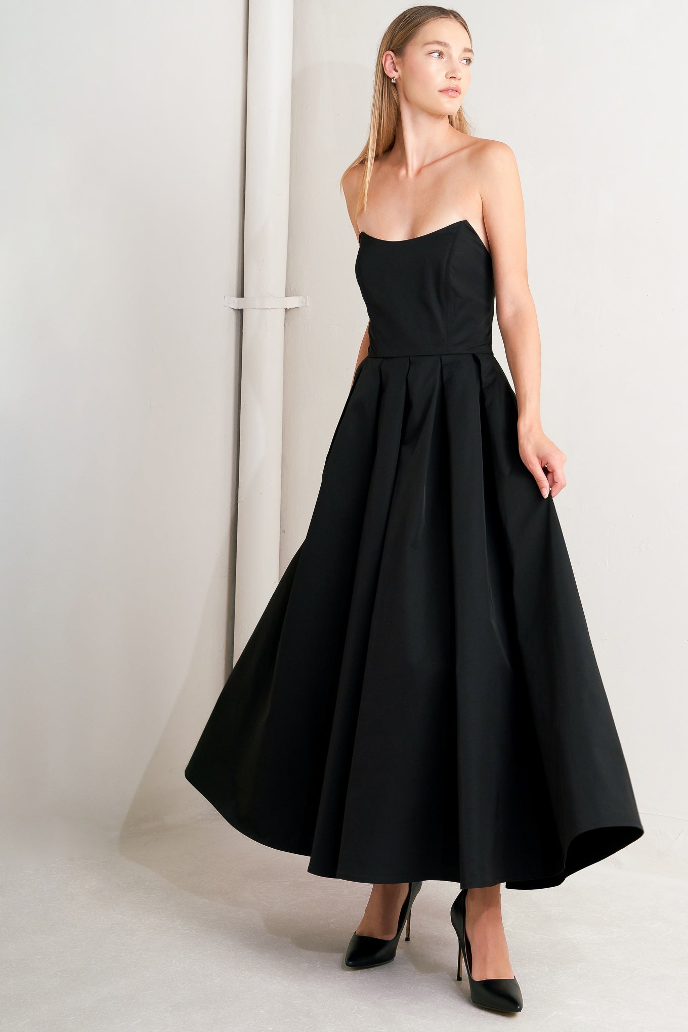 A solid woven midi dress featuring strapless with pointed side neckline, full skirt and back zipper closure