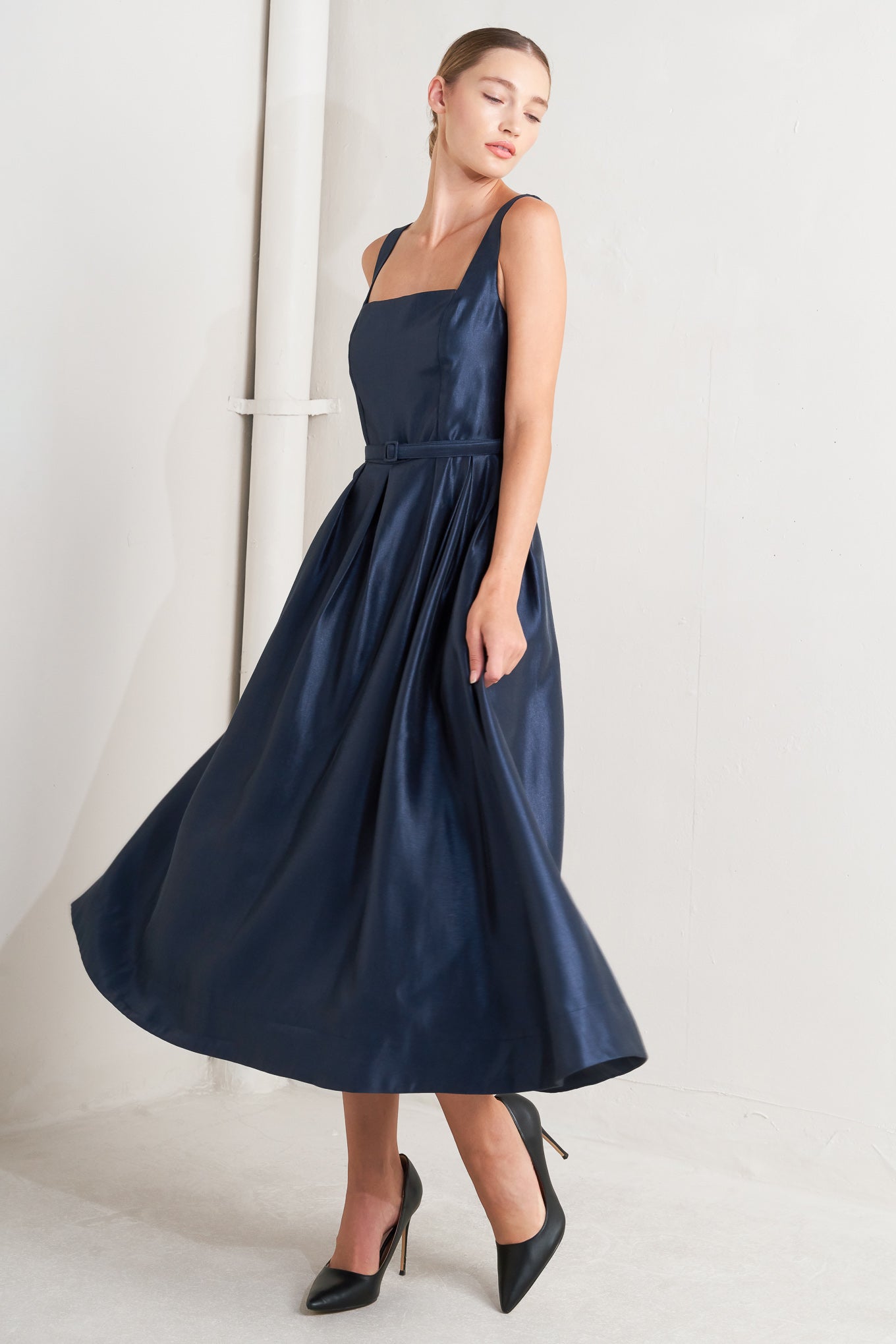 A solid woven midi dress featuring straight neckline, sleeveless, self belt, full skirt and back zipper closure