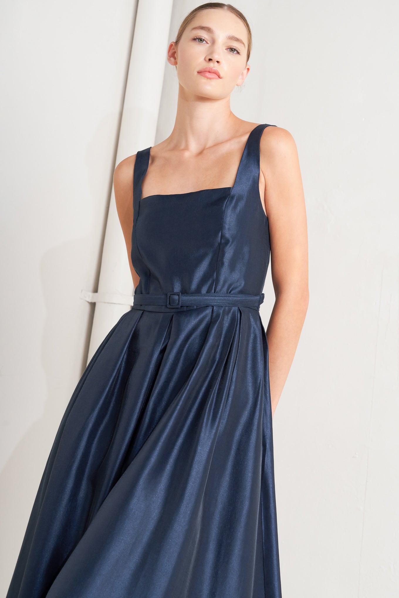 A solid woven midi dress featuring straight neckline, sleeveless, self belt, full skirt and back zipper closure