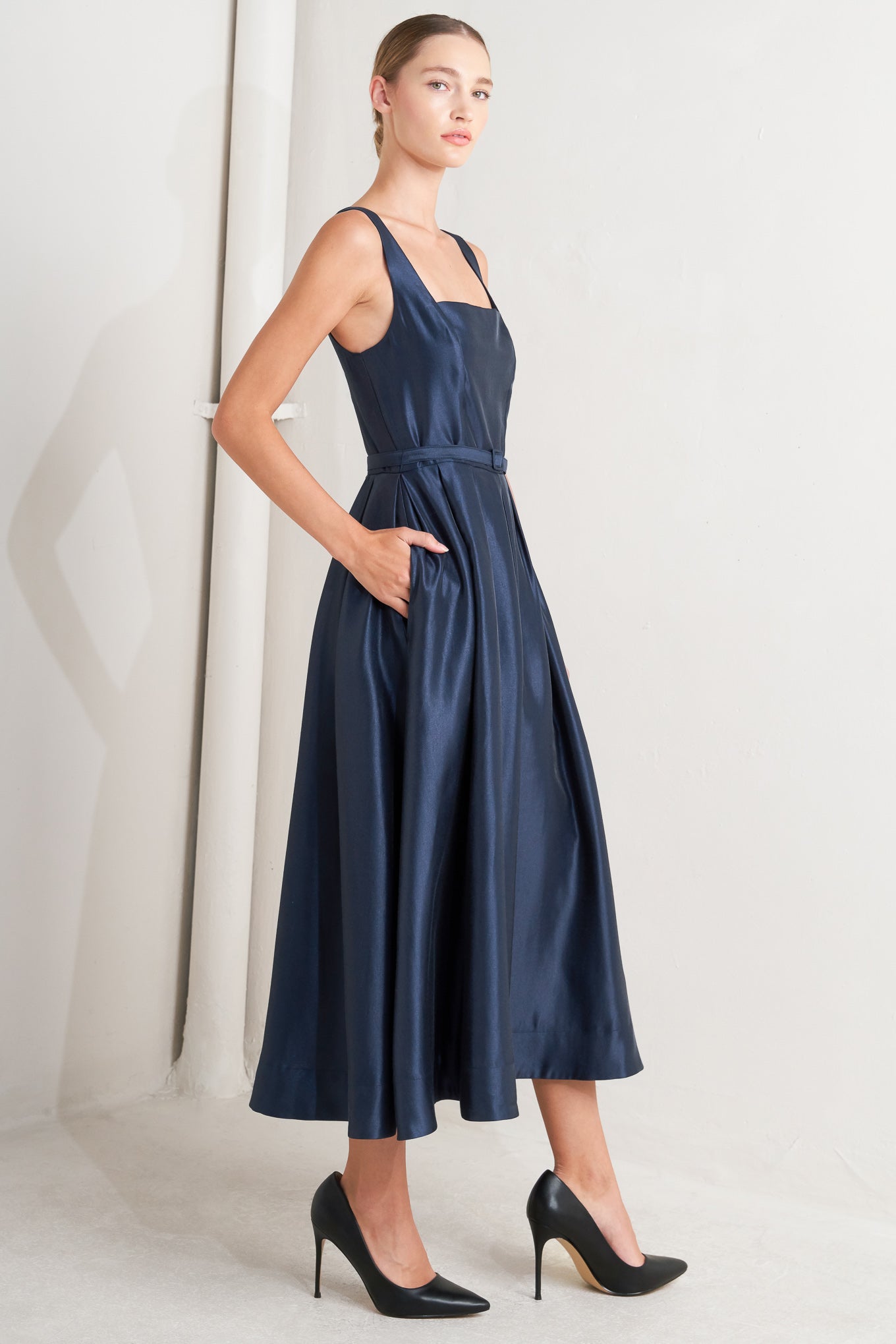 A solid woven midi dress featuring straight neckline, sleeveless, self belt, full skirt and back zipper closure
