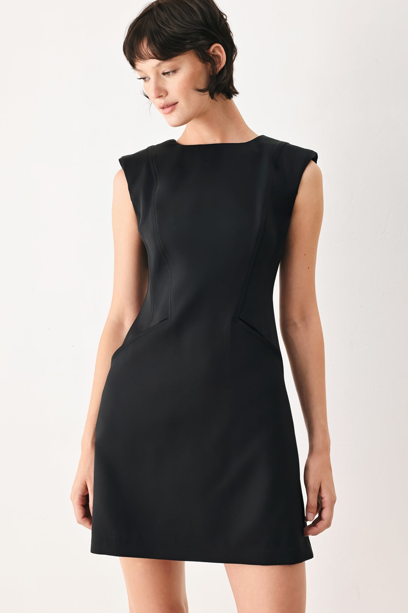 Woman wearing a black shift mini dress featuring wide round neckline, cap sleeve, pockets and back zipper closure | FREEMARKET