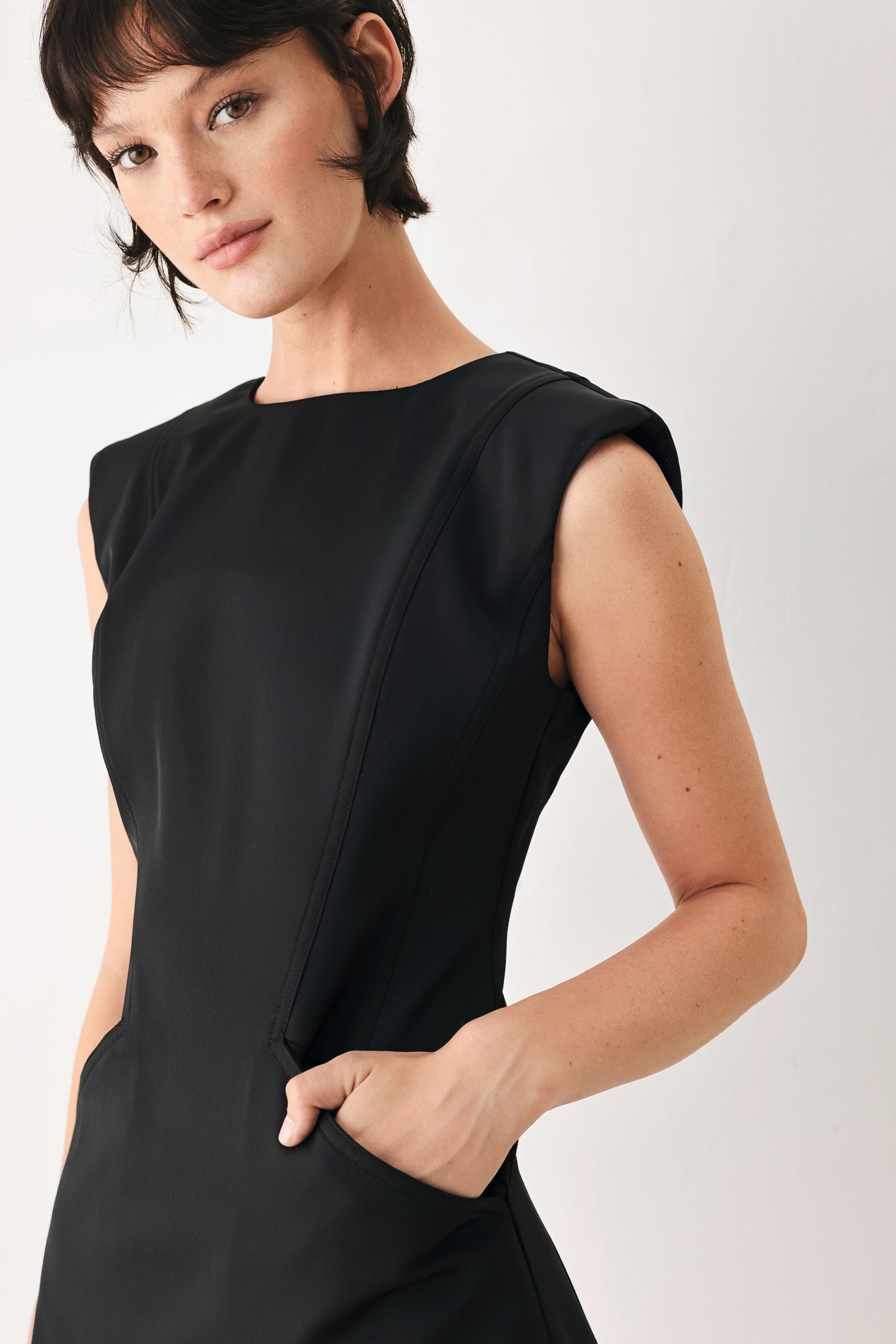 Woman wearing a black shift mini dress featuring wide round neckline, cap sleeve, pockets and back zipper closure | FREEMARKET