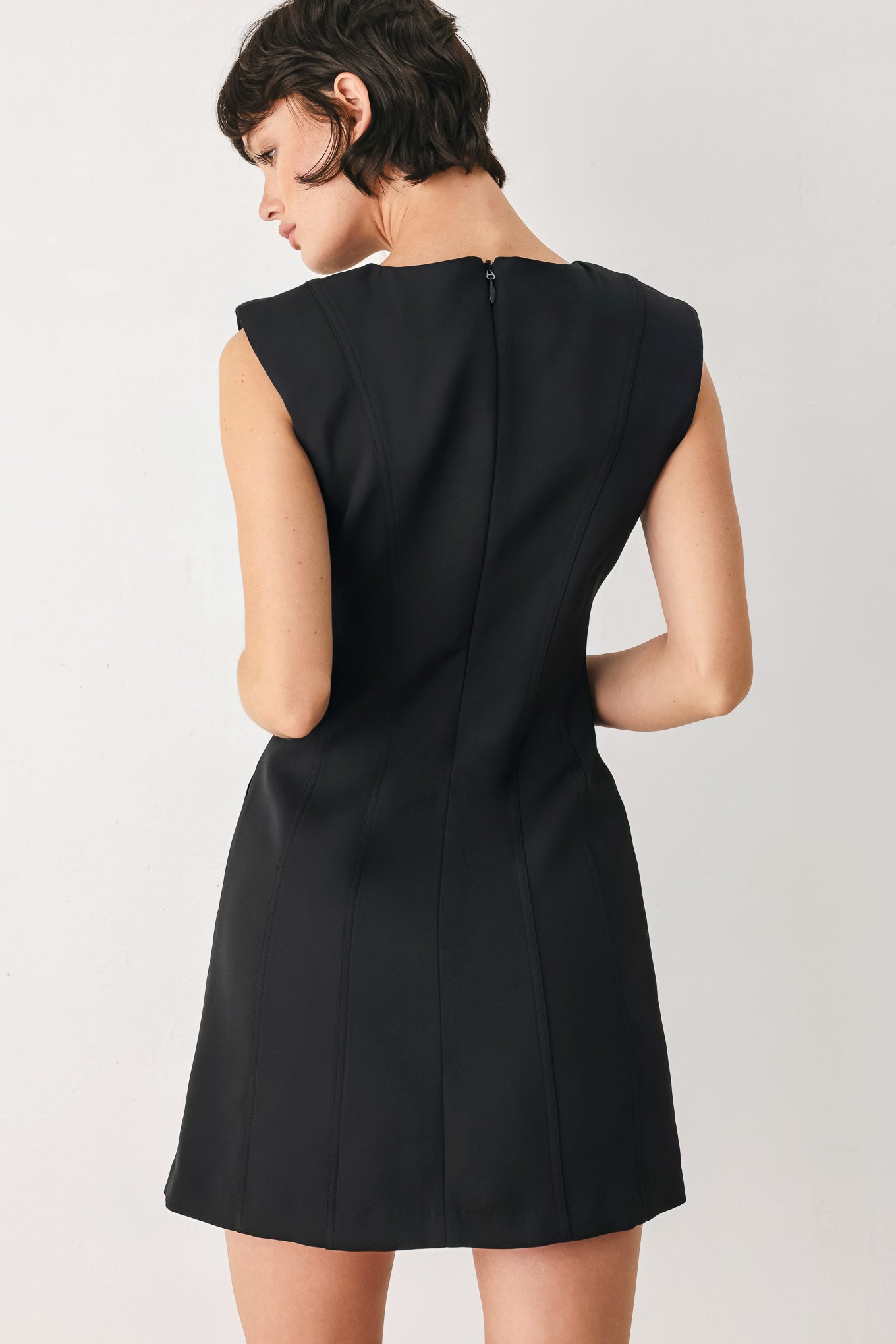 Woman wearing a black shift mini dress featuring wide round neckline, cap sleeve, pockets and back zipper closure | FREEMARKET