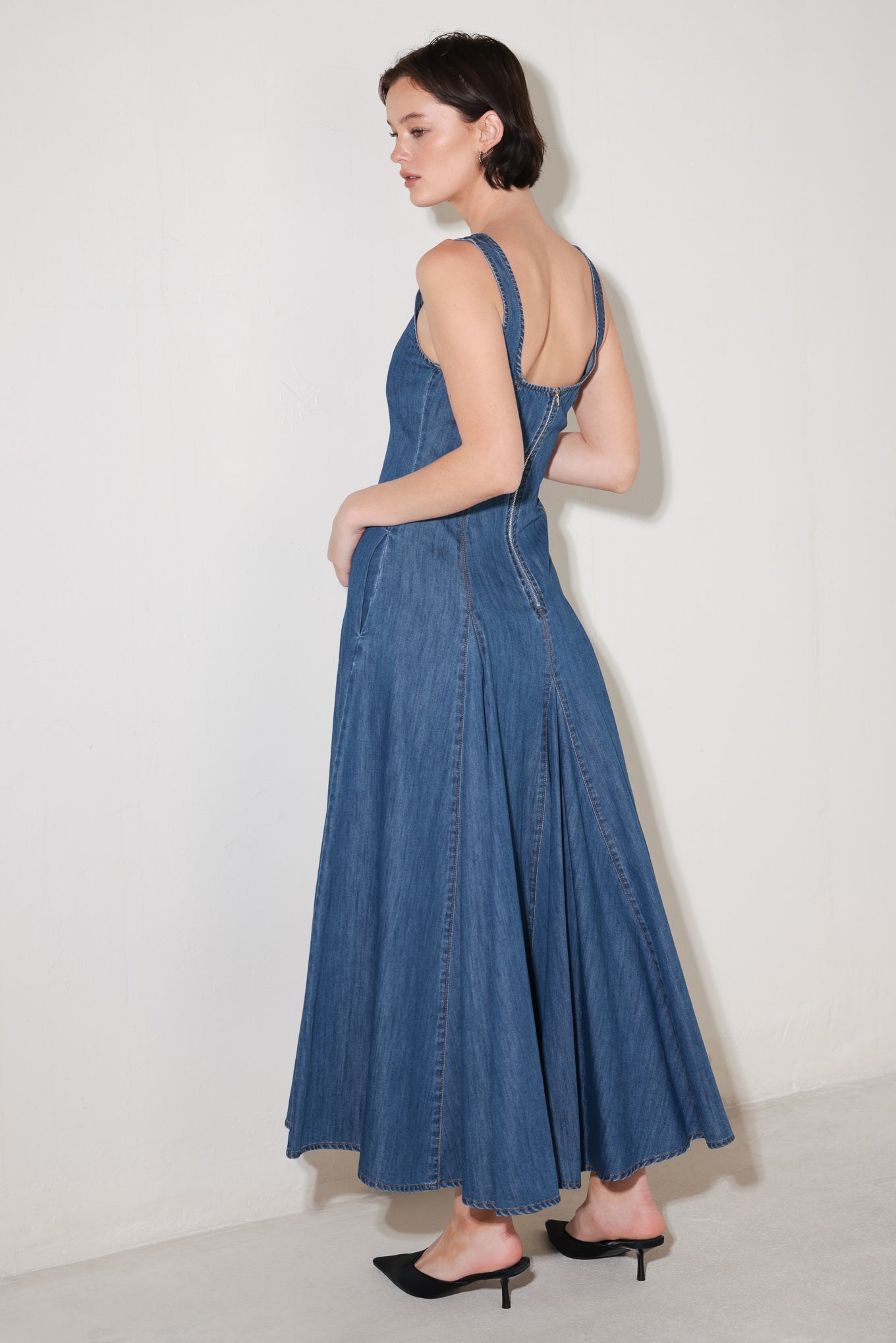 Woman wearing a blue sleeveless denim midi dress featuring square neckline, circle skirt and low back with zipper closure | FREEMARKET | Flying Tomato