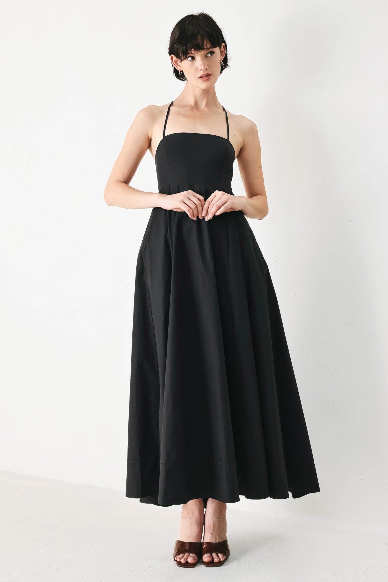 Woman wearing black midi dress featuring straight neckline, circle skirt and bare back with lace up tie closure | Flying Tomato
