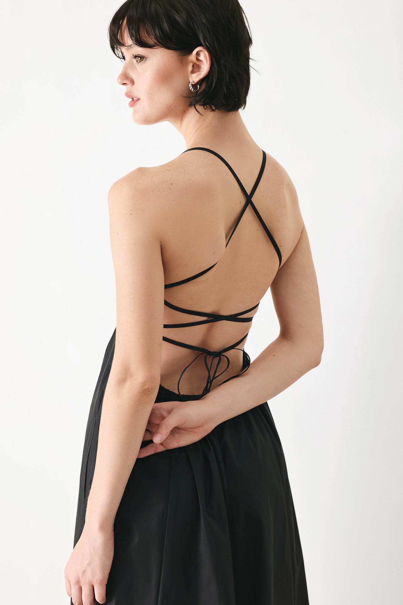 Woman wearing black midi dress featuring straight neckline, circle skirt and bare back with lace up tie closure | Flying Tomato