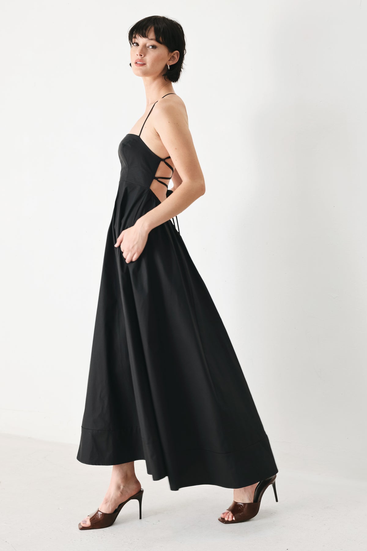 Woman wearing black midi dress featuring straight neckline, circle skirt and bare back with lace up tie closure | Flying Tomato