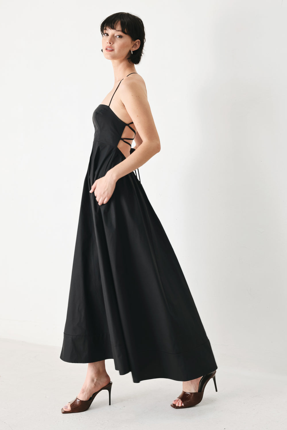Woman wearing black midi dress featuring straight neckline, circle skirt and bare back with lace up tie closure | Flying Tomato