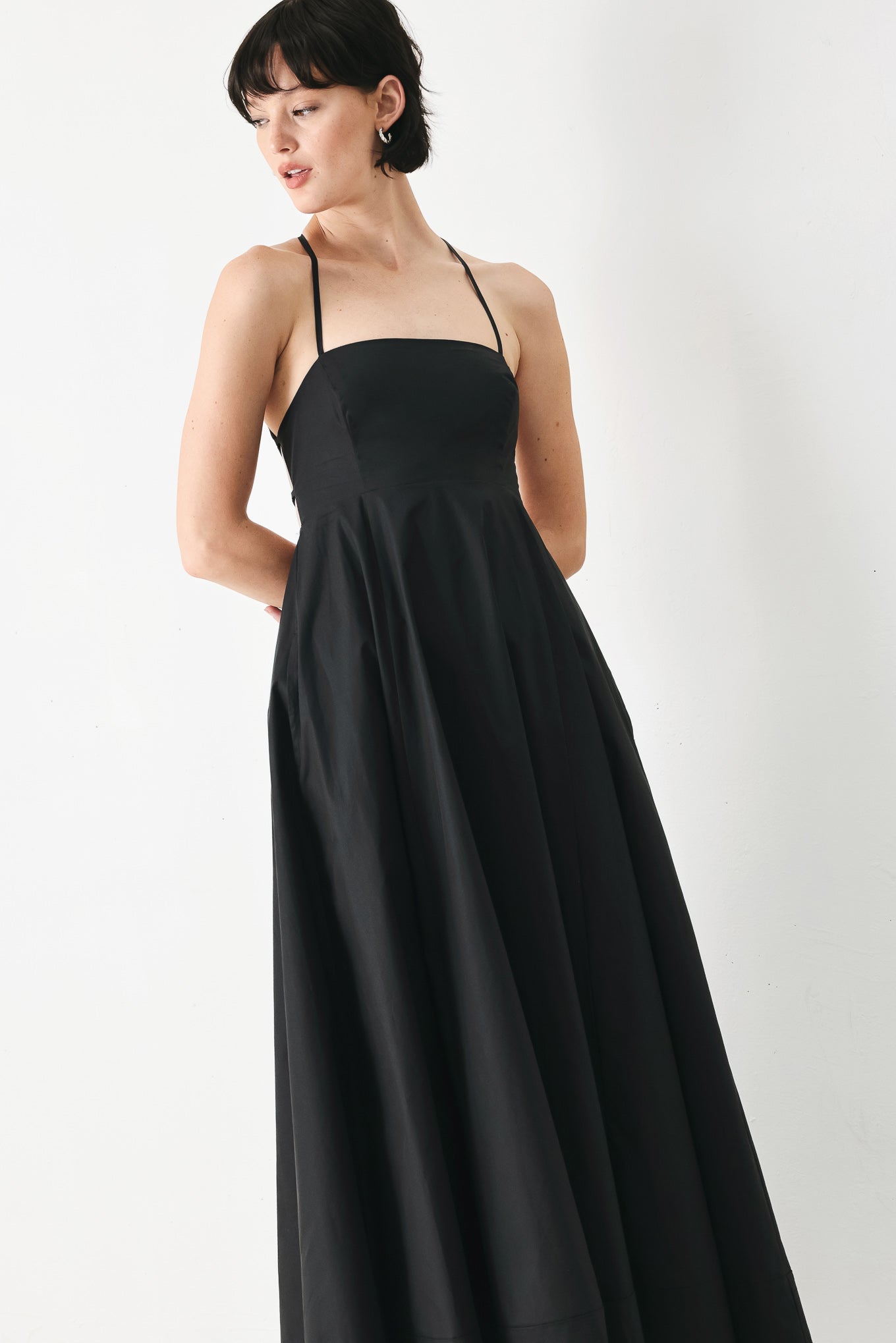 Woman wearing black midi dress featuring straight neckline, circle skirt and bare back with lace up tie closure | Flying Tomato