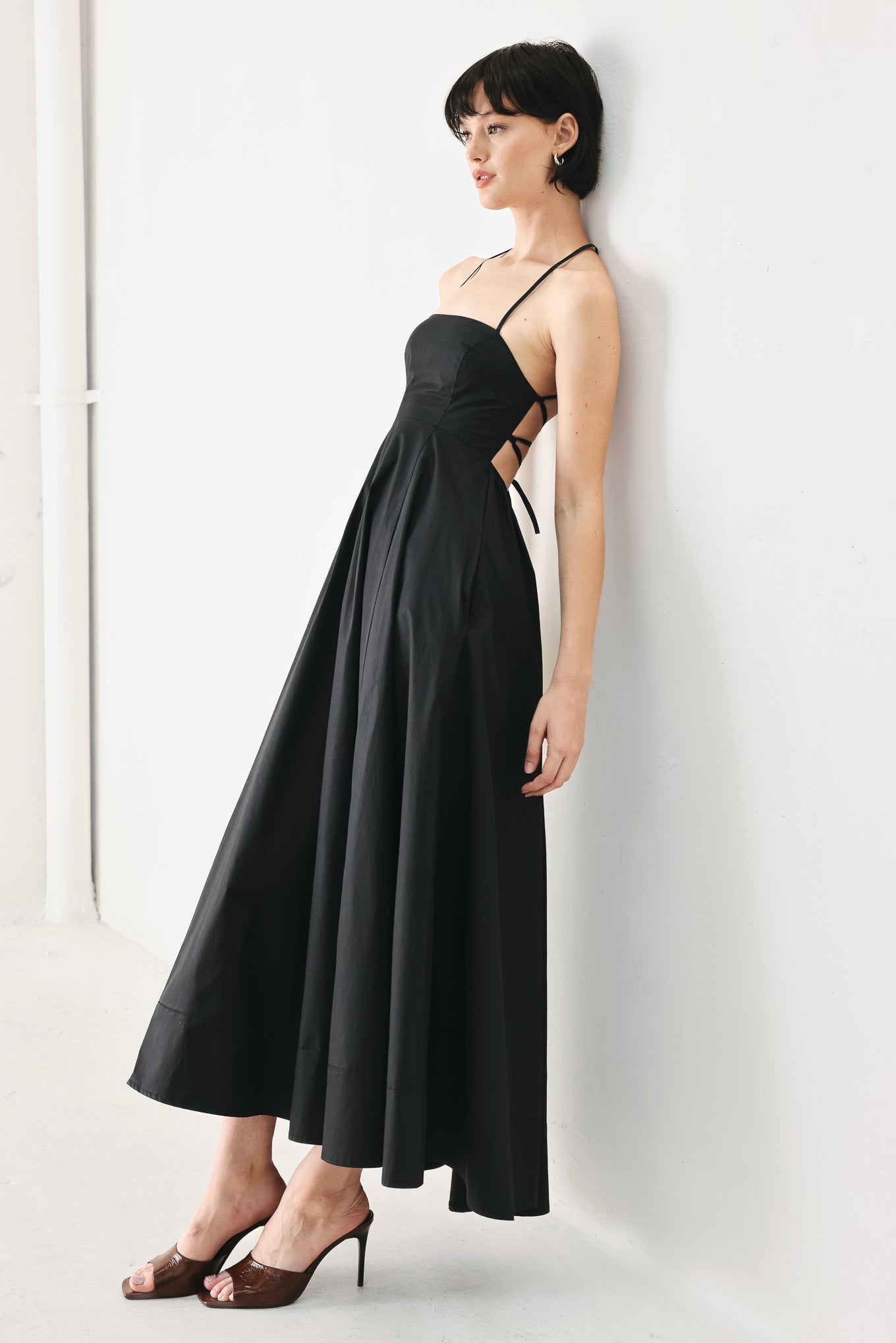 Woman wearing black midi dress featuring straight neckline, circle skirt and bare back with lace up tie closure | Flying Tomato