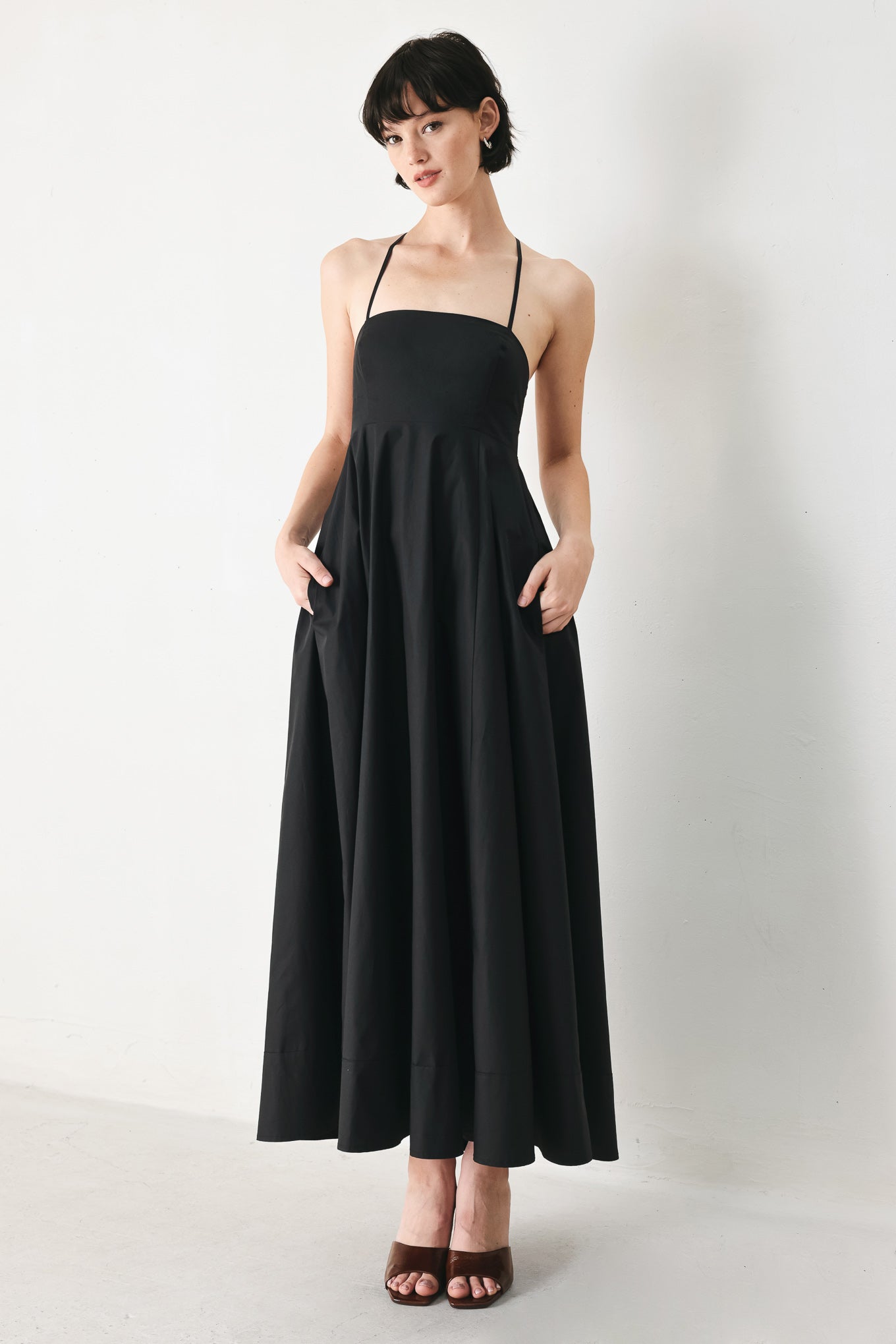 Woman wearing black midi dress featuring straight neckline, circle skirt and bare back with lace up tie closure | Flying Tomato