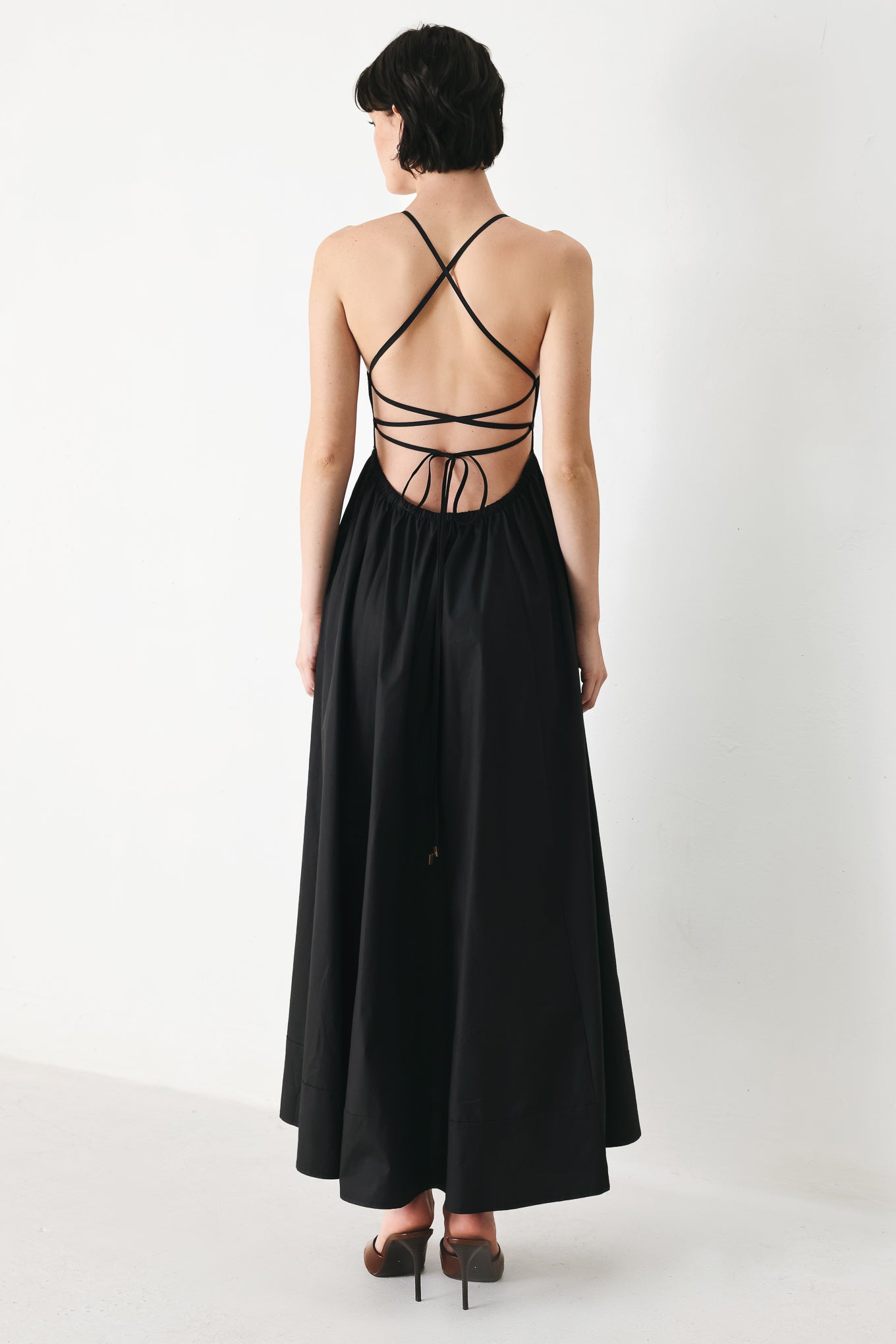 Woman wearing black midi dress featuring straight neckline, circle skirt and bare back with lace up tie closure | Flying Tomato