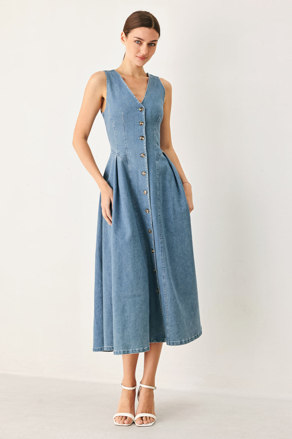 Woman wearing a sleeveless blue denim midi dress with V neckline, button down, and side pleat | FREEMARKET