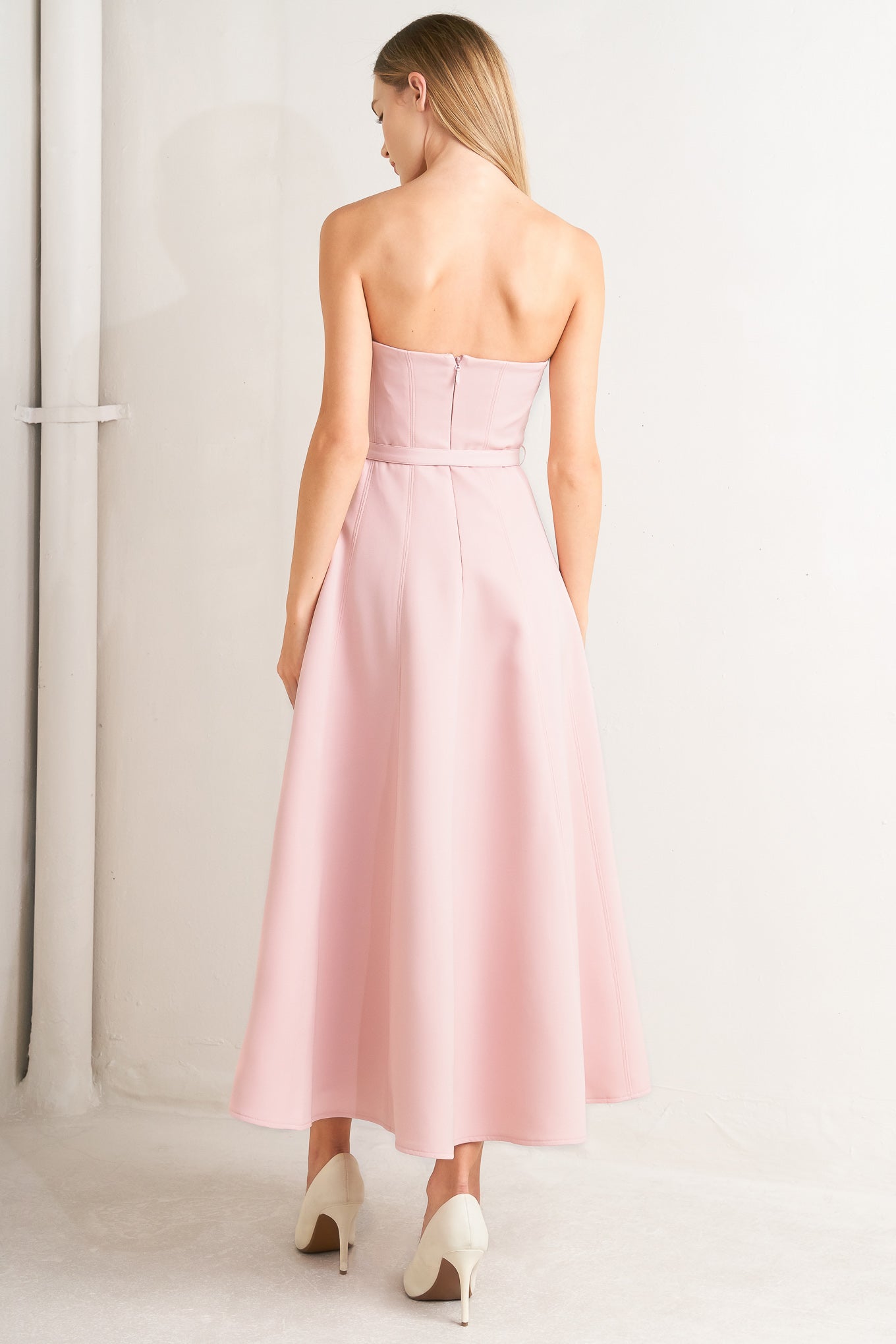 A solid woven midi dress featuring strapless with V front, self belt, circle skirt and back zipper closure