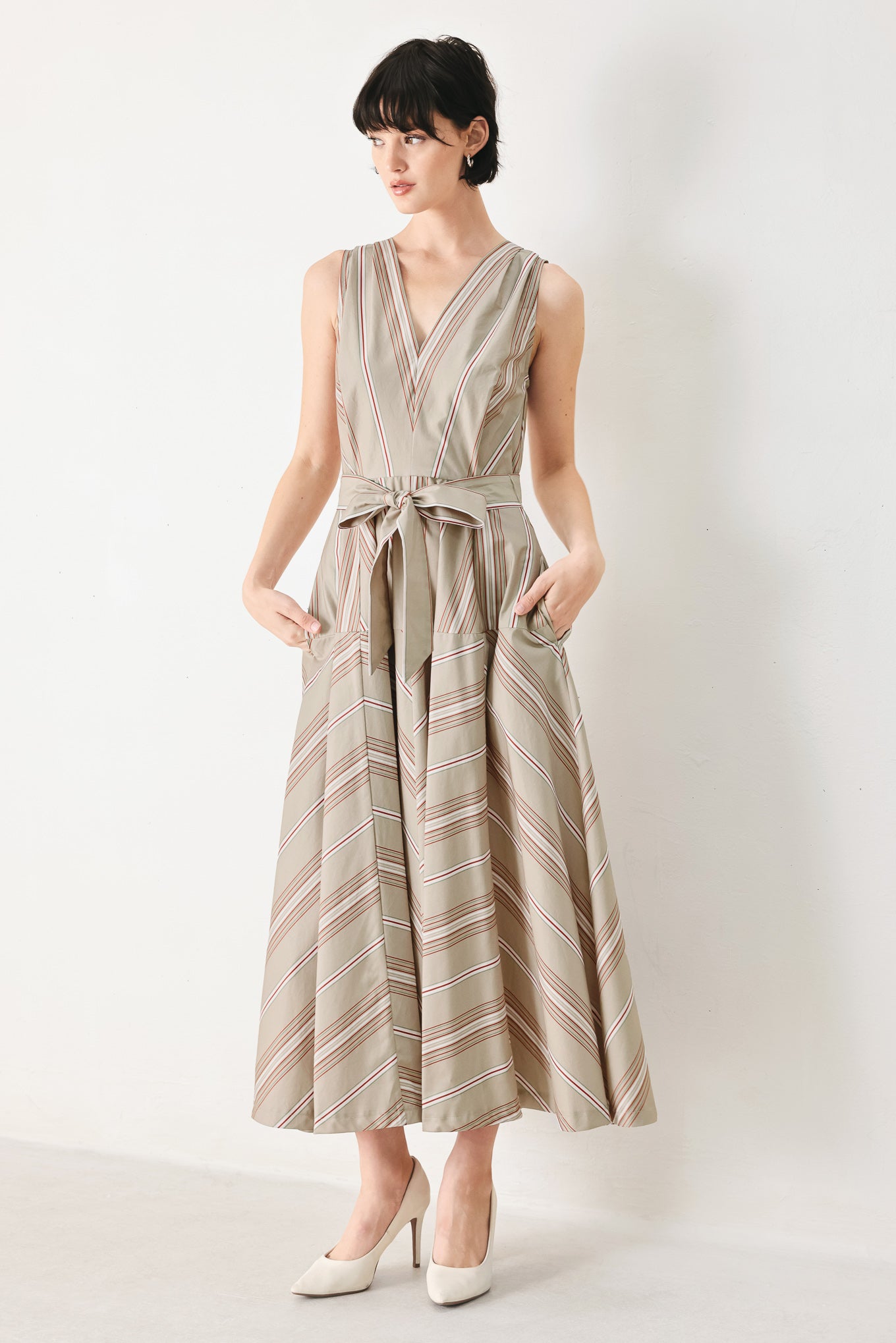 Woman wearing a striped sleeveless woven midi dress featuring V neckline, drop waist, self tie, circle skirt and back zipper closure | FREEMARKET