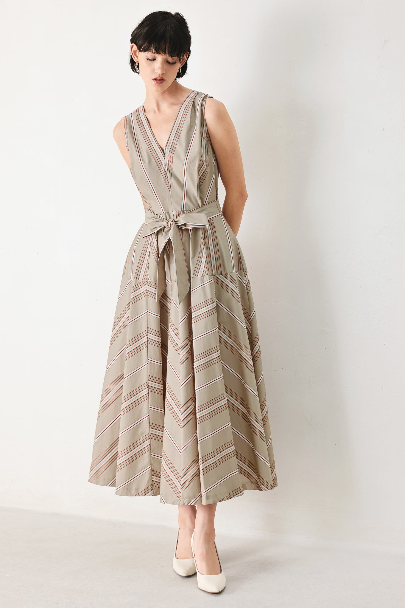 Woman wearing a striped sleeveless woven midi dress featuring V neckline, drop waist, self tie, circle skirt and back zipper closure | FREEMARKET