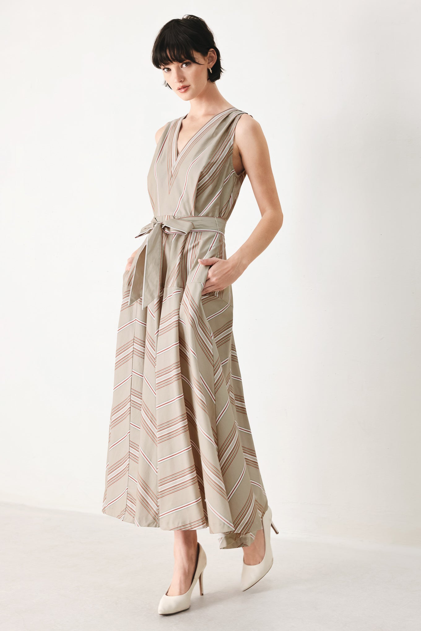 Woman wearing a striped sleeveless woven midi dress featuring V neckline, drop waist, self tie, circle skirt and back zipper closure | FREEMARKET