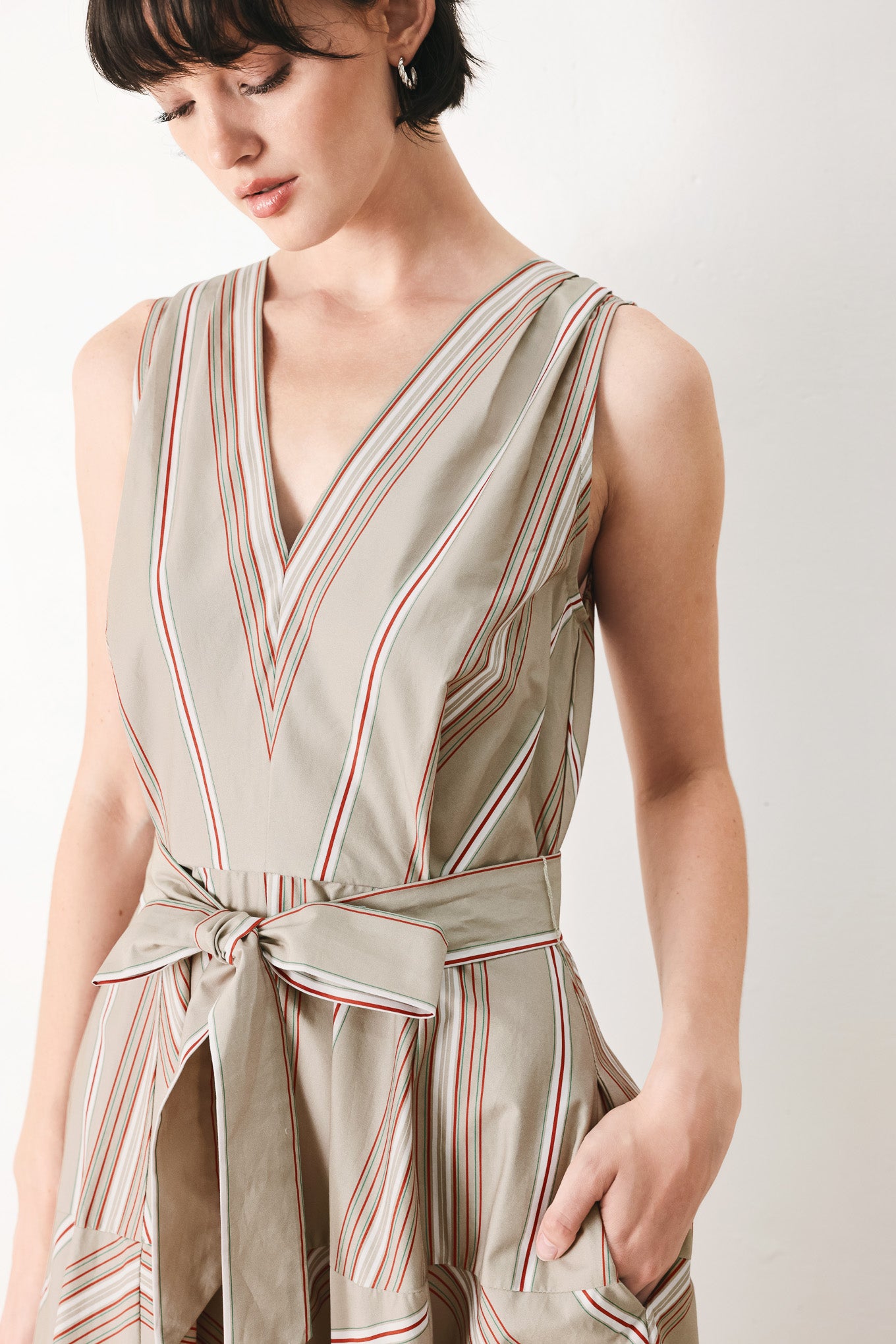 Woman wearing a striped sleeveless woven midi dress featuring V neckline, drop waist, self tie, circle skirt and back zipper closure | FREEMARKET