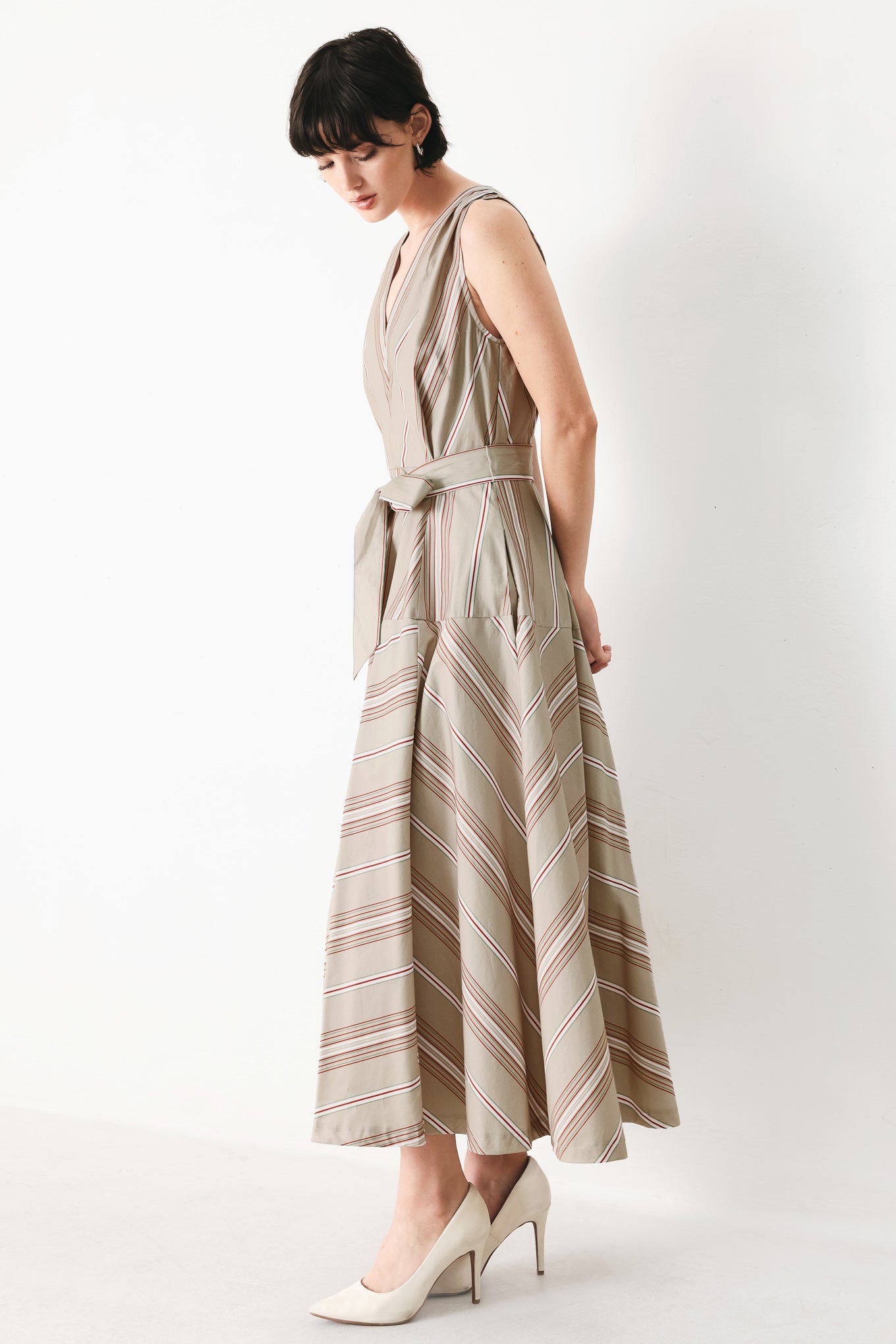 Woman wearing a striped sleeveless woven midi dress featuring V neckline, drop waist, self tie, circle skirt and back zipper closure | FREEMARKET