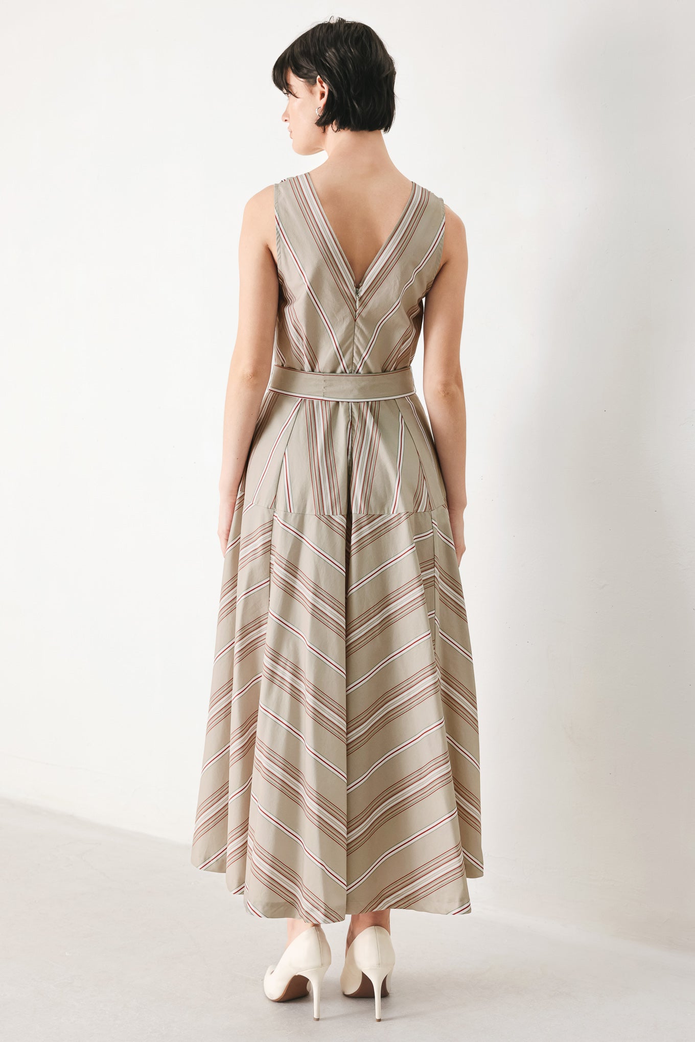 Woman wearing a striped sleeveless woven midi dress featuring V neckline, drop waist, self tie, circle skirt and back zipper closure | FREEMARKET