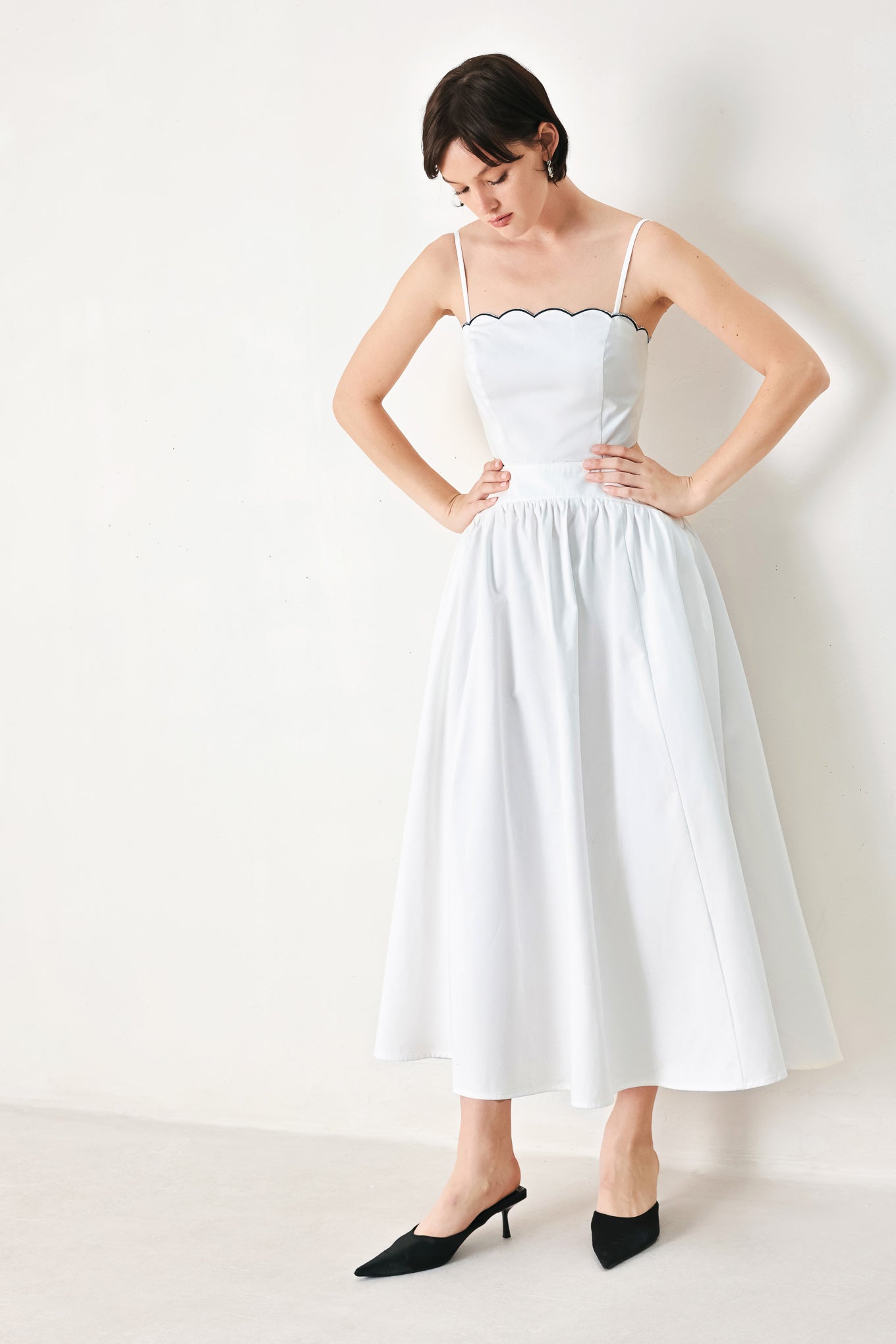 A solid woven midi dress featuring scalloped neckline, straps, side cut out, full skirt, smocked back bodice with zipper closure