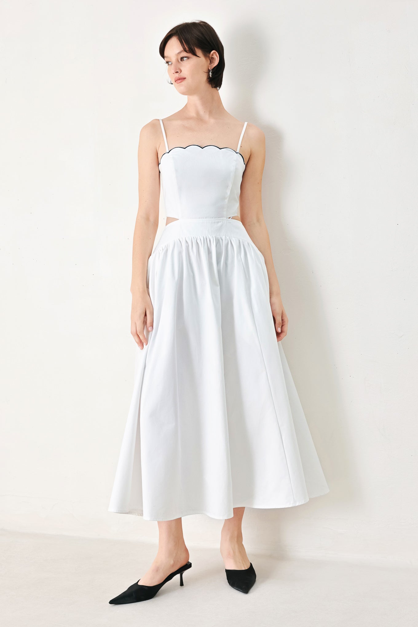 A solid woven midi dress featuring scalloped neckline, straps, side cut out, full skirt, smocked back bodice with zipper closure