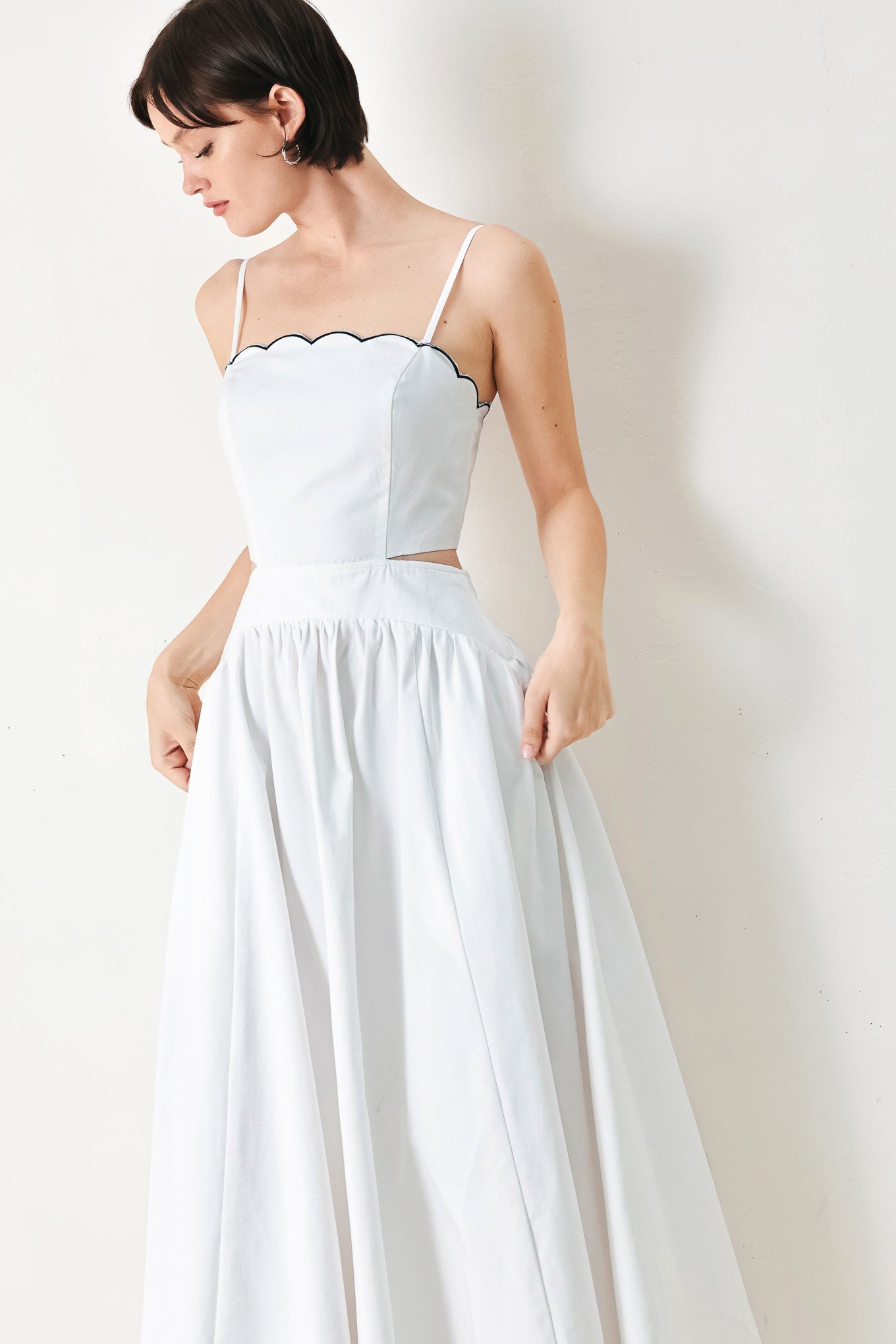 A solid woven midi dress featuring scalloped neckline, straps, side cut out, full skirt, smocked back bodice with zipper closure