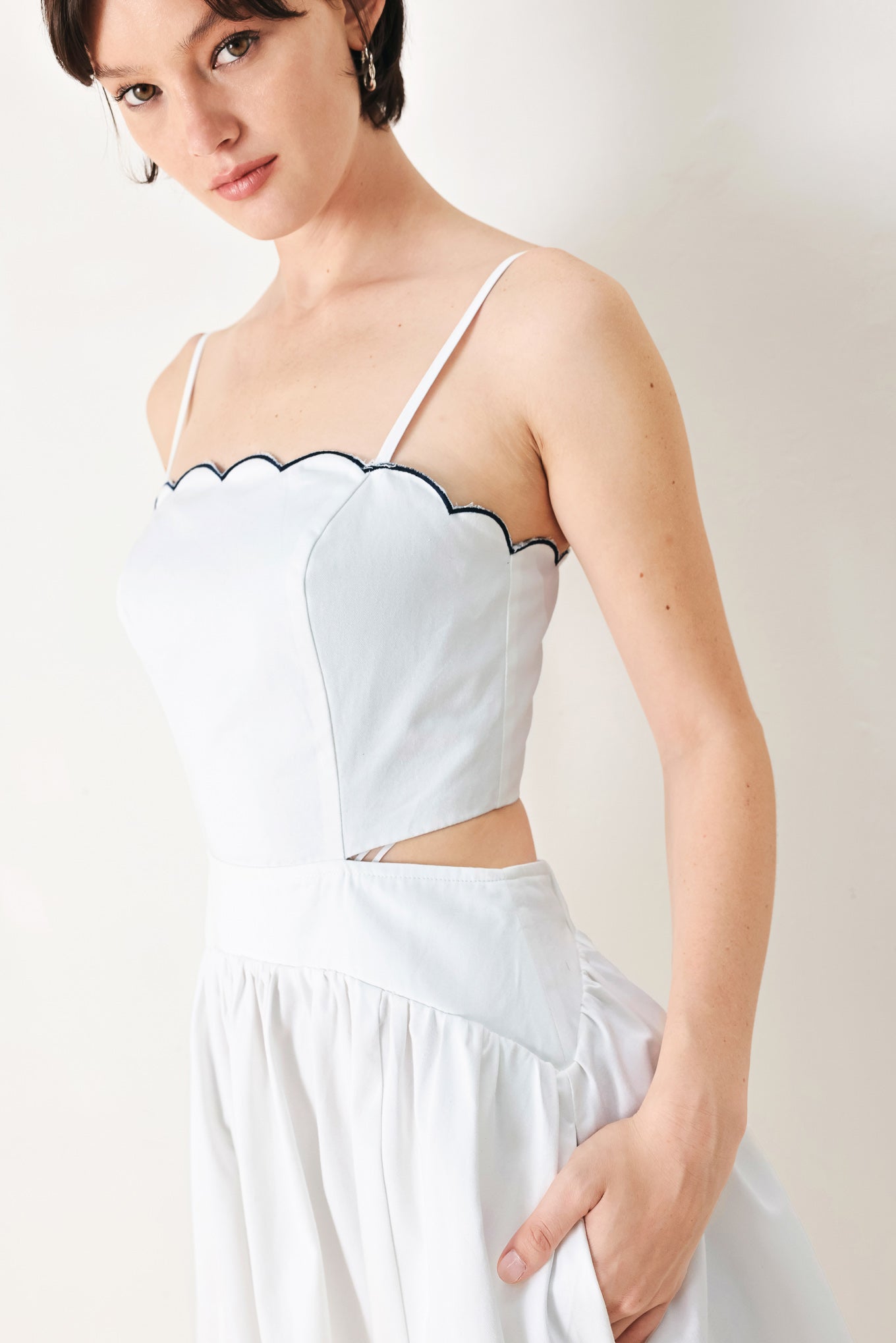 A solid woven midi dress featuring scalloped neckline, straps, side cut out, full skirt, smocked back bodice with zipper closure