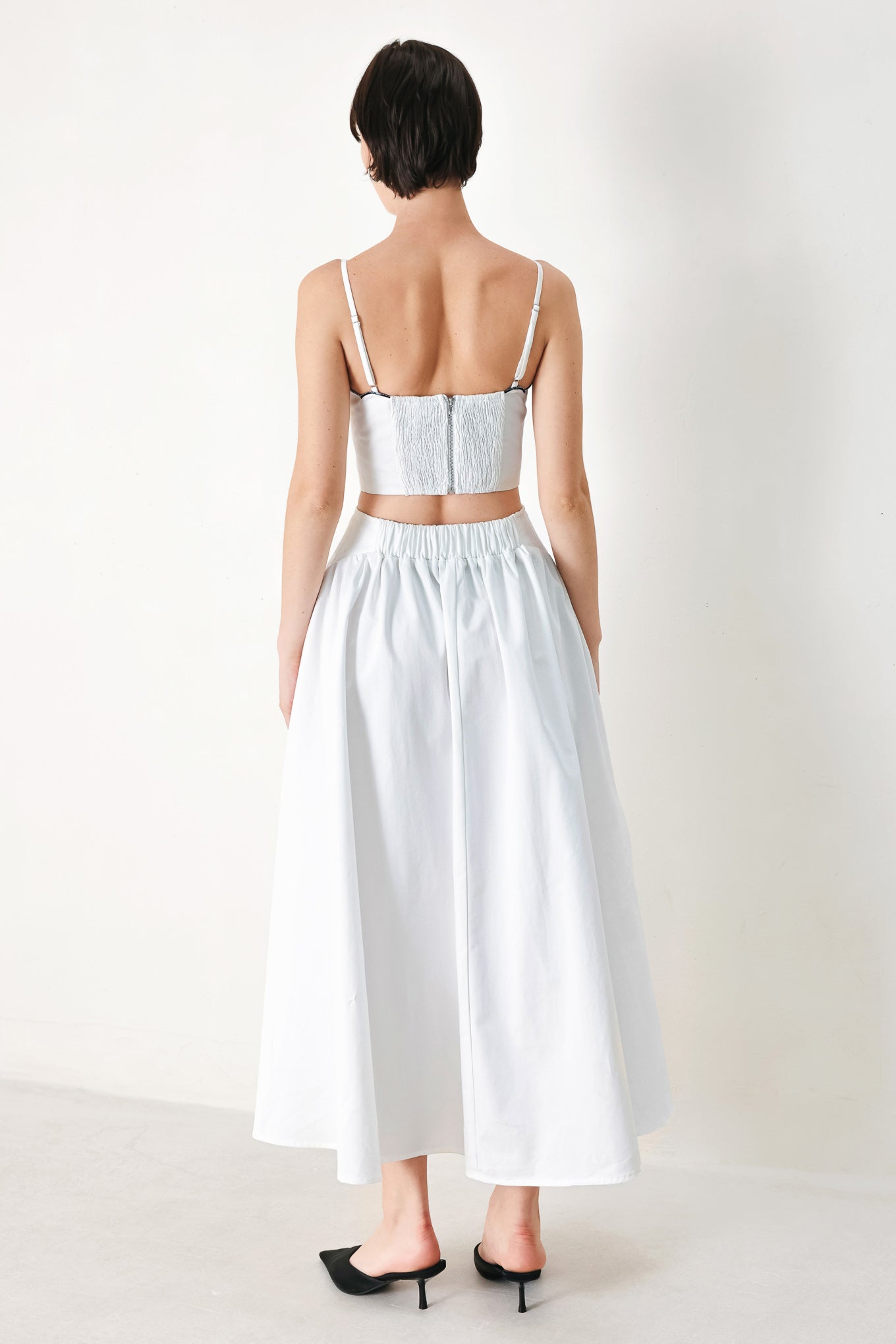 A solid woven midi dress featuring scalloped neckline, straps, side cut out, full skirt, smocked back bodice with zipper closure