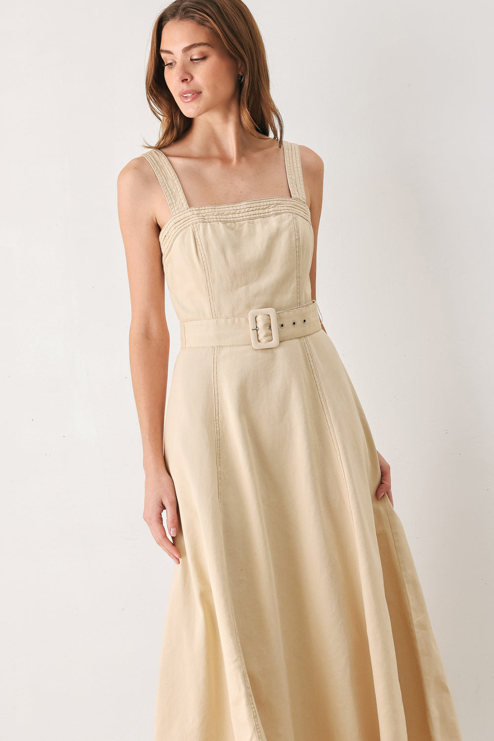 A woman modeling a sleeveless midi dress in a light beige or neutral color, featuring a square neckline, a matching belt at the waist, and a flared skirt | FREEMARKET