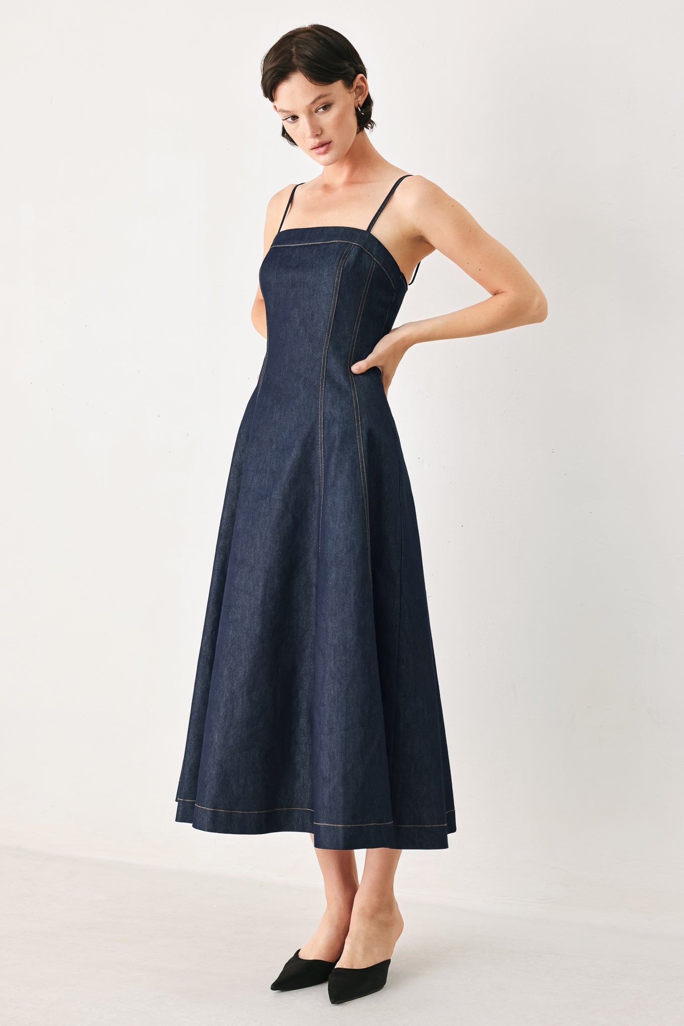 Woman wearing a navy blue denim midi dress with straight neckline, straps, full circle skirt and back zipper closure | FREEMARKET
