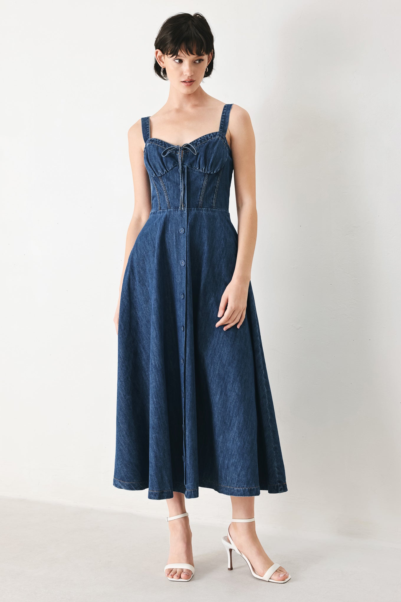 Woman wearing an indigo blue denim midi dress featuring sweetheart neckline with tie, straps, corset waist, front button detail, circle skirt and back zipper closure | FREEMARKET