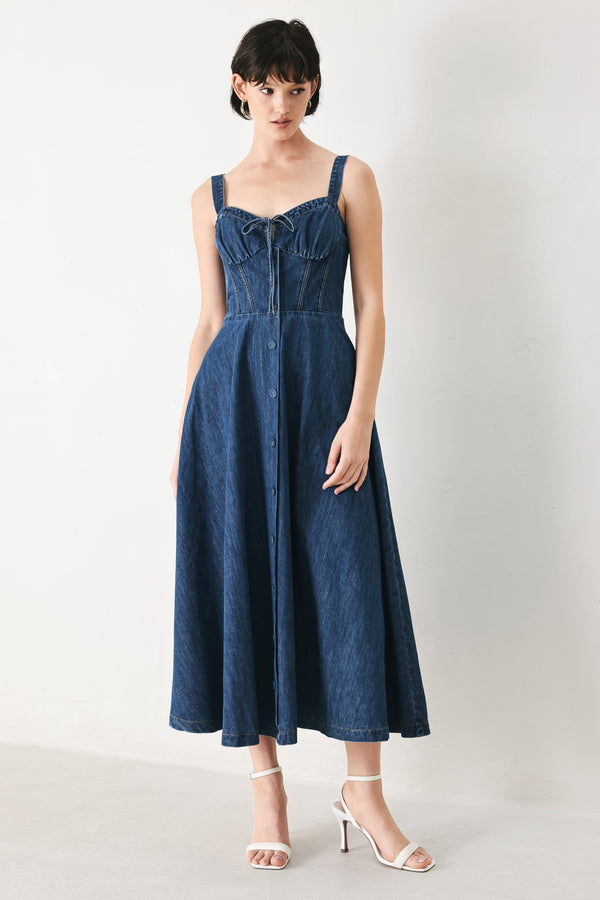 Woman wearing an indigo blue denim midi dress featuring sweetheart neckline with tie, straps, corset waist, front button detail, circle skirt and back zipper closure | FREEMARKET
