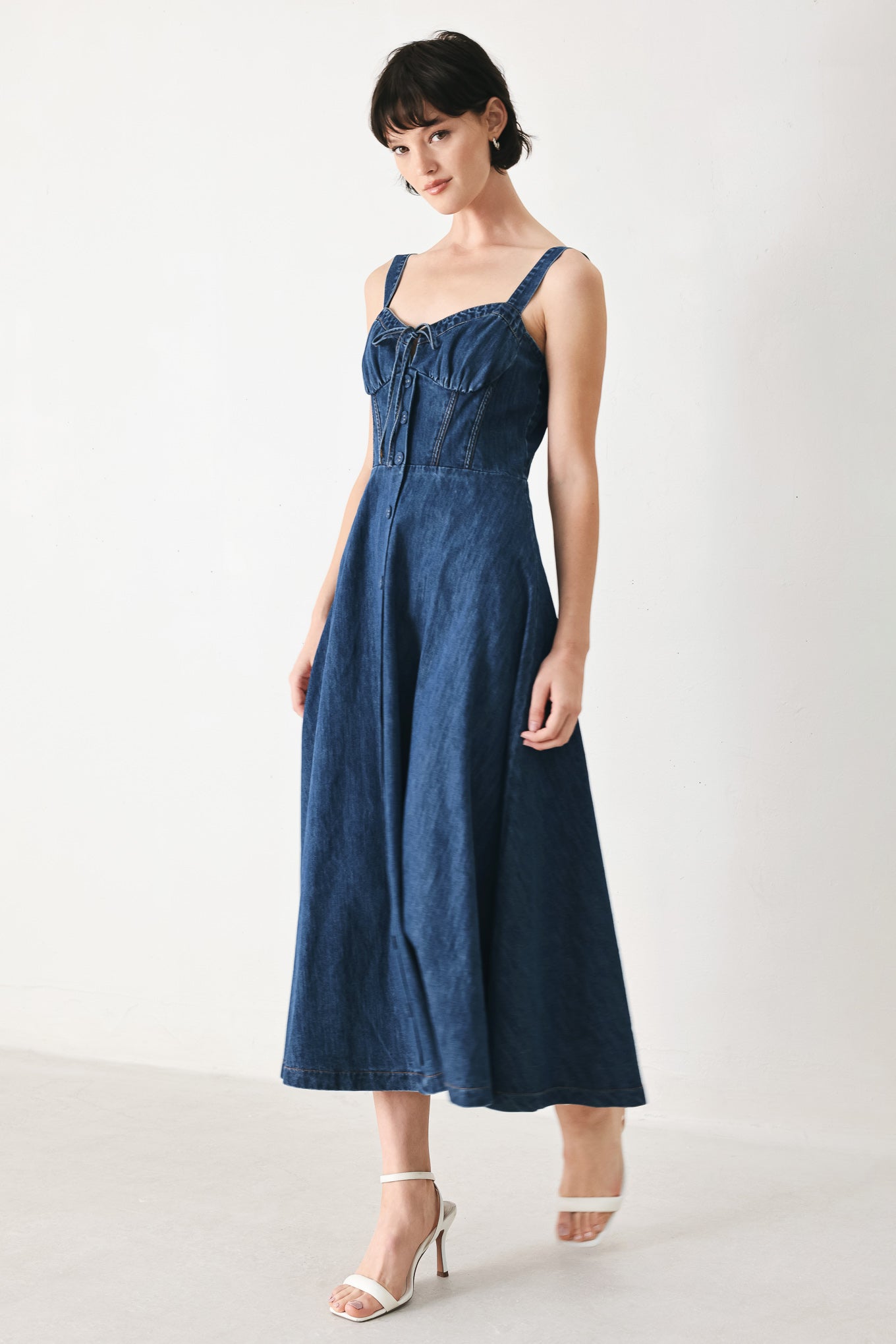 Woman wearing an indigo blue denim midi dress featuring sweetheart neckline with tie, straps, corset waist, front button detail, circle skirt and back zipper closure | FREEMARKET