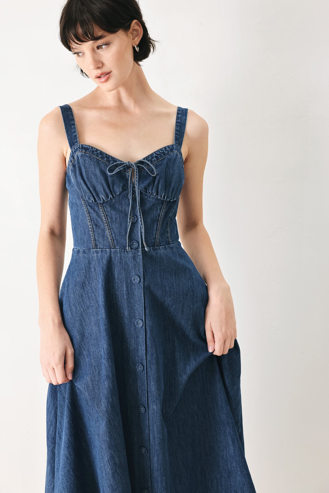Woman wearing an indigo blue denim midi dress featuring sweetheart neckline with tie, straps, corset waist, front button detail, circle skirt and back zipper closure | FREEMARKET