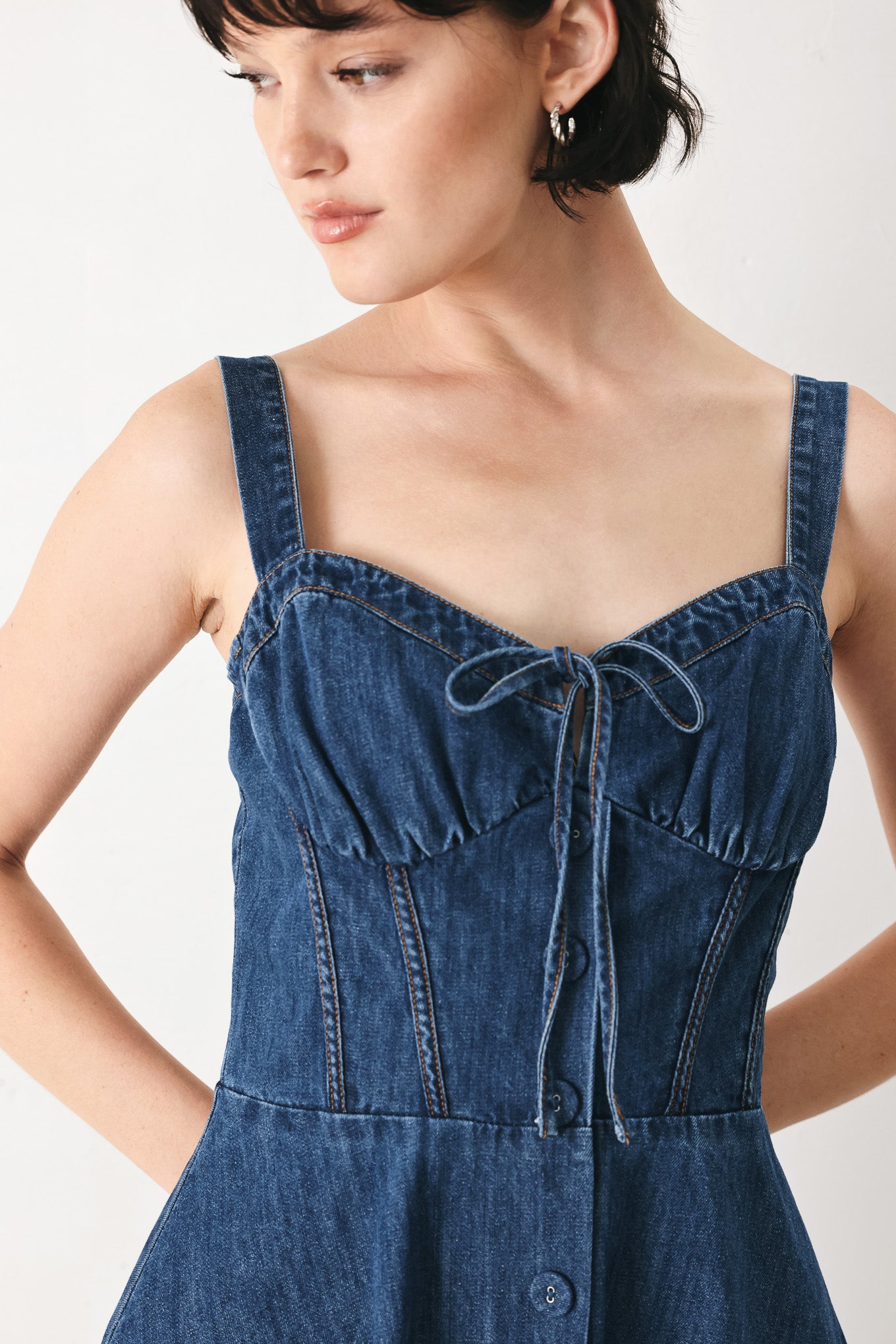 Woman wearing an indigo blue denim midi dress featuring sweetheart neckline with tie, straps, corset waist, front button detail, circle skirt and back zipper closure | FREEMARKET