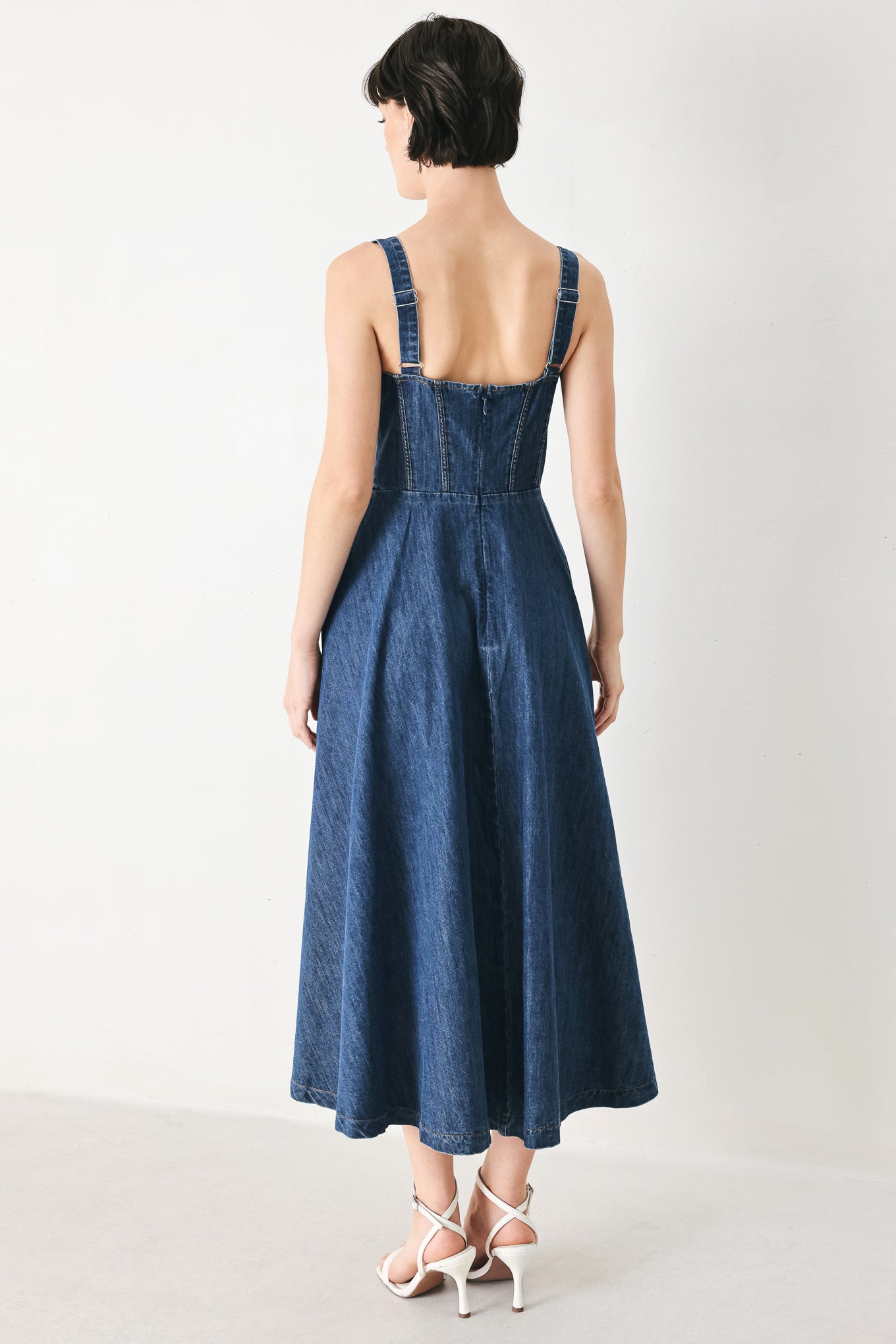 Woman wearing an indigo blue denim midi dress featuring sweetheart neckline with tie, straps, corset waist, front button detail, circle skirt and back zipper closure | FREEMARKET