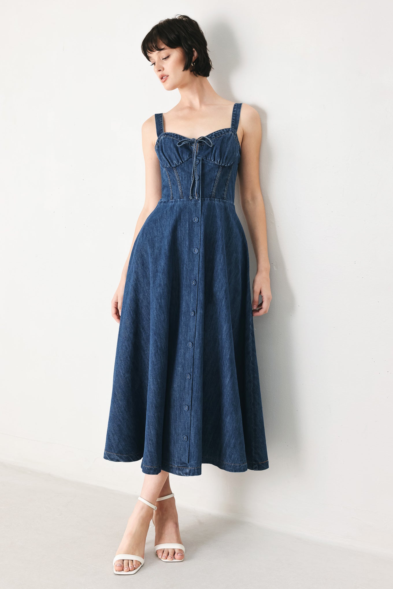 Woman wearing an indigo blue denim midi dress featuring sweetheart neckline with tie, straps, corset waist, front button detail, circle skirt and back zipper closure | FREEMARKET