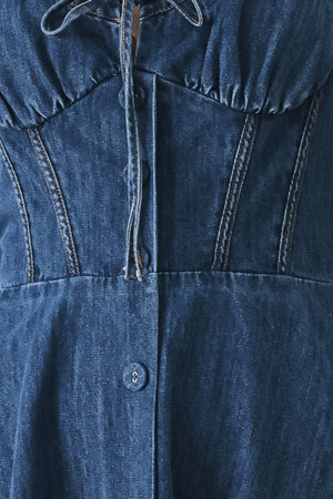 Close up of an indigo blue denim midi dress featuring sweetheart neckline with tie, straps, corset waist, front button detail, circle skirt and back zipper closure | FREEMARKET