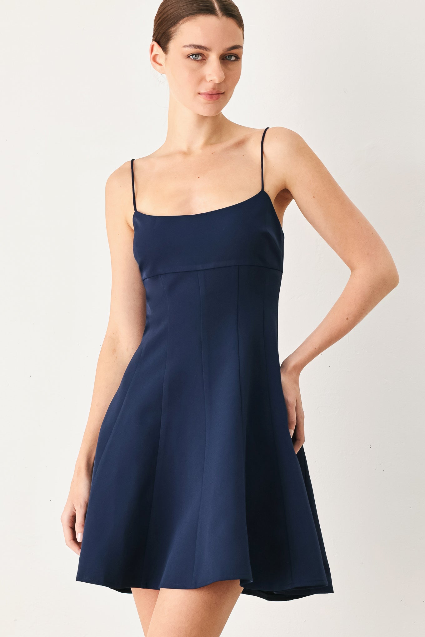 A woman wearing a navy spaghetti-strap mini dress with a structured bodice and flared skirt | Flying Tomato