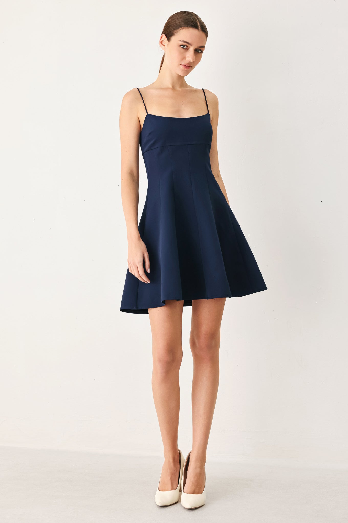 A woman wearing a navy spaghetti-strap mini dress with a structured bodice and flared skirt | Flying Tomato