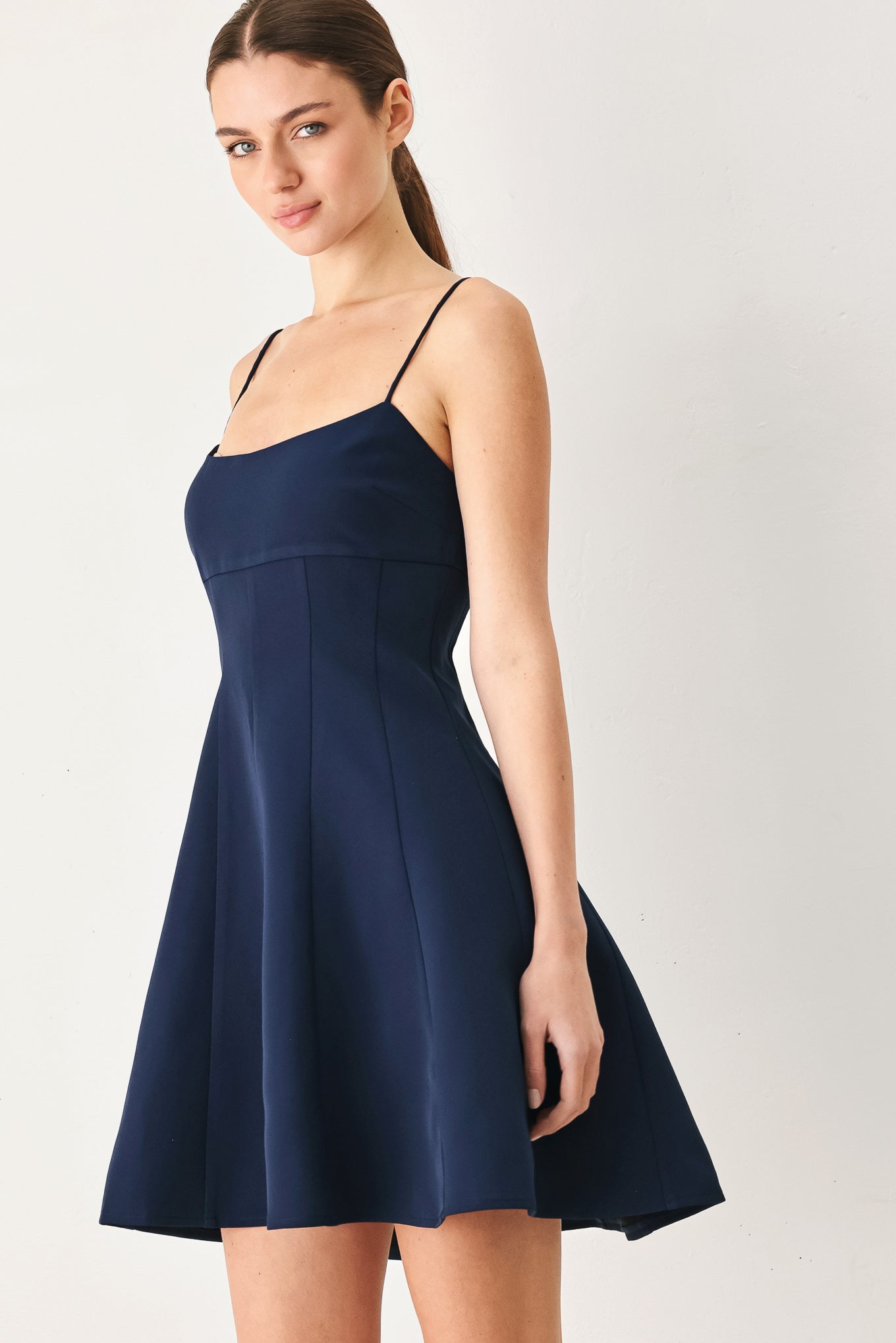 A woman wearing a navy spaghetti-strap mini dress with a structured bodice and flared skirt | Flying Tomato