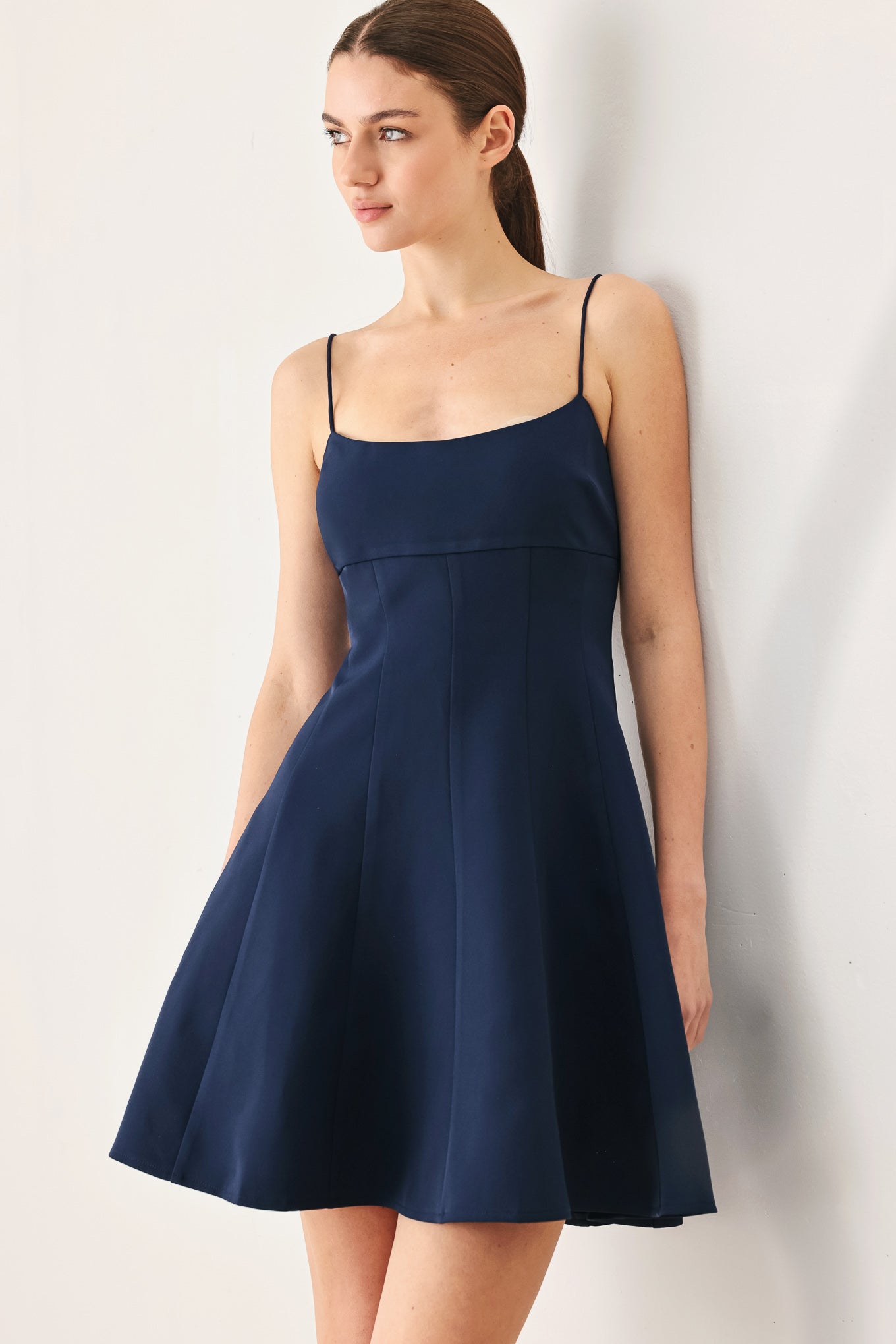 A woman wearing a navy spaghetti-strap mini dress with a structured bodice and flared skirt | Flying Tomato