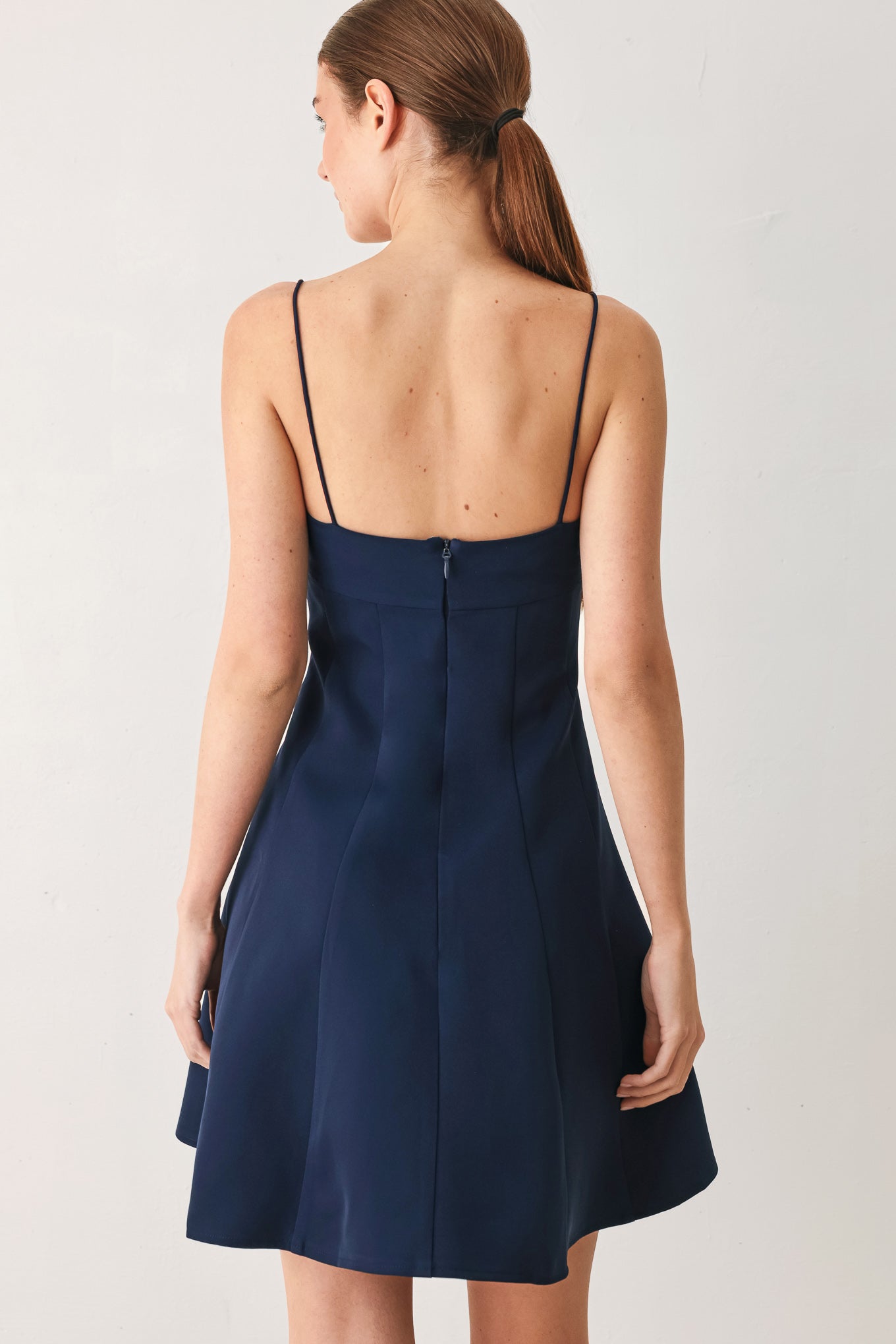 A woman wearing a navy spaghetti-strap mini dress with a structured bodice and flared skirt | Flying Tomato
