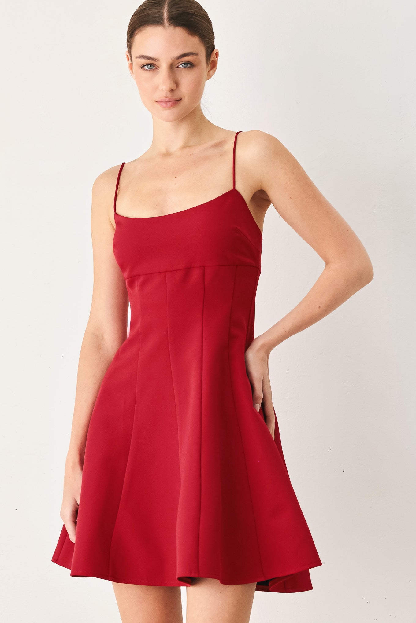 A woman wearing a red spaghetti-strap mini dress with a structured bodice and flared skirt | Flying Tomato