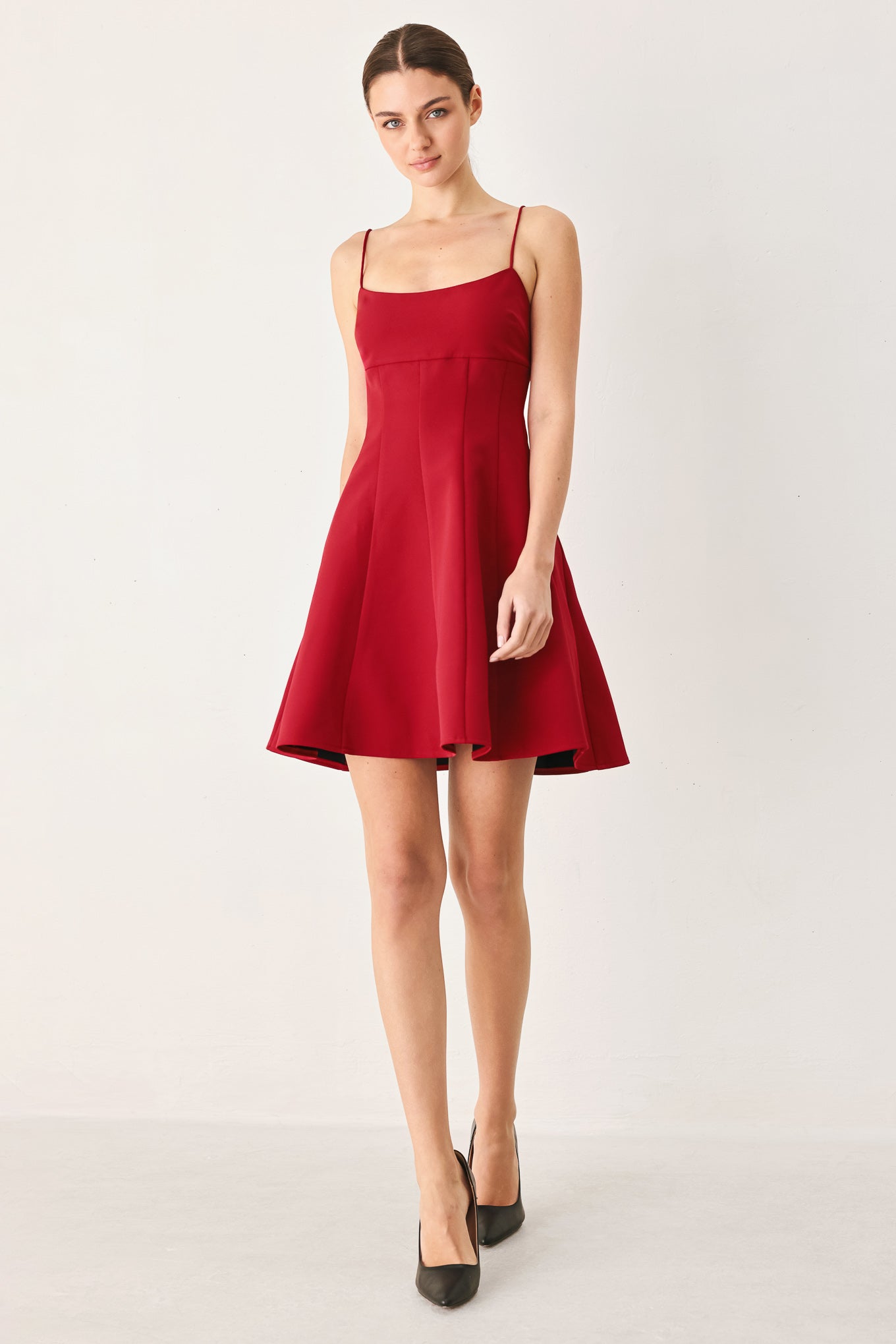 A woman wearing a red spaghetti-strap mini dress with a structured bodice and flared skirt | Flying Tomato