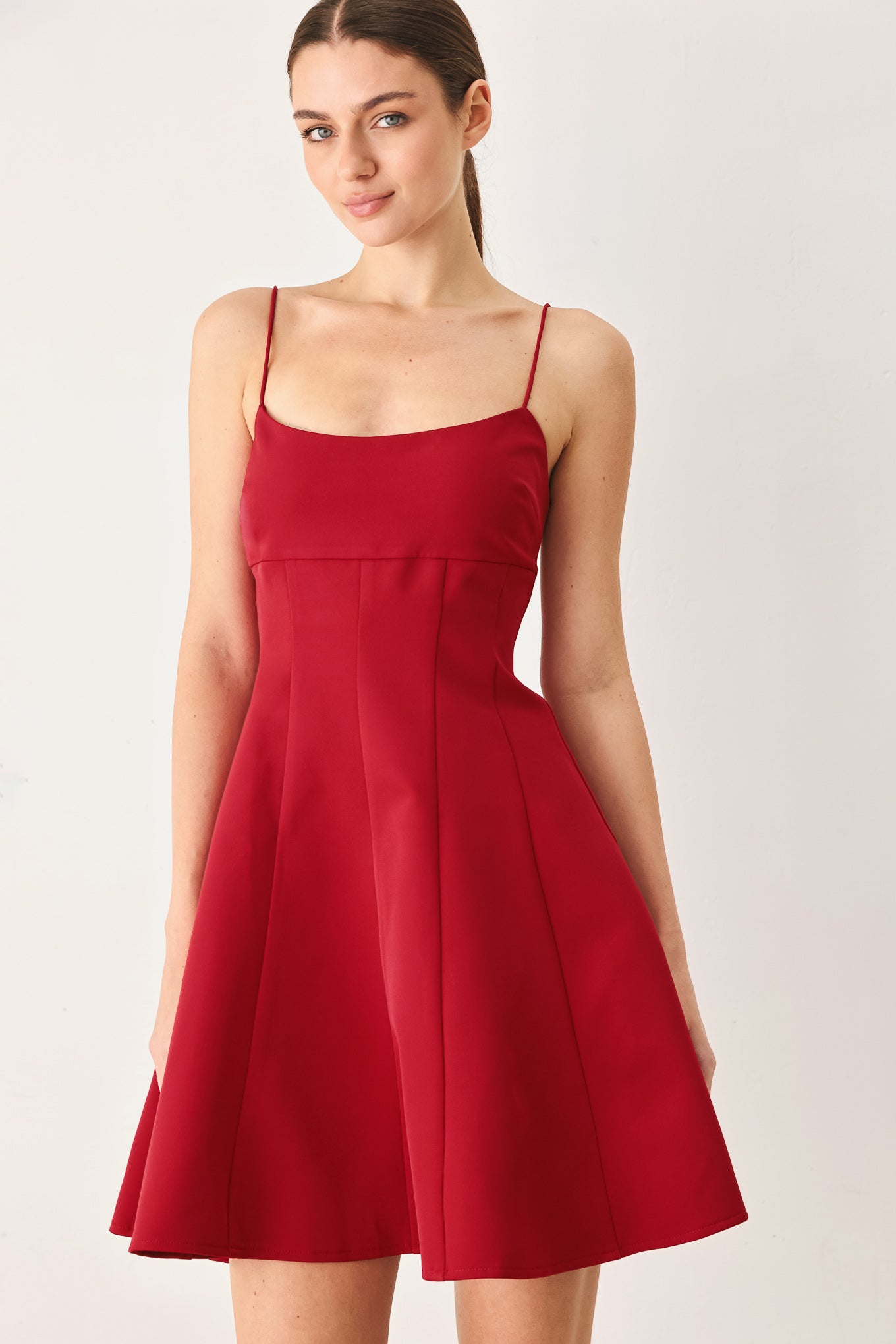A woman wearing a red spaghetti-strap mini dress with a structured bodice and flared skirt | Flying Tomato
